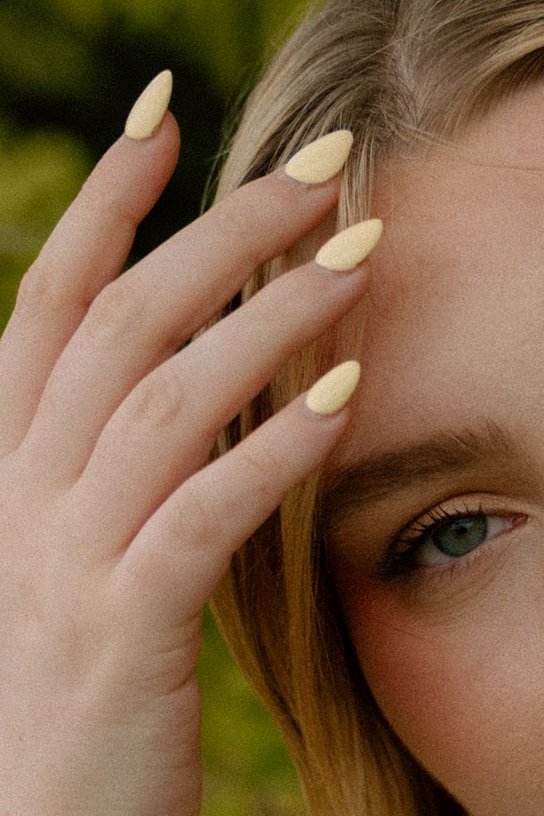Close-up of pale yellow almond-shaped nails and eye.
