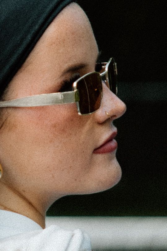 Side profile view of someone wearing stylish rectangular sunglasses and a dark head covering.