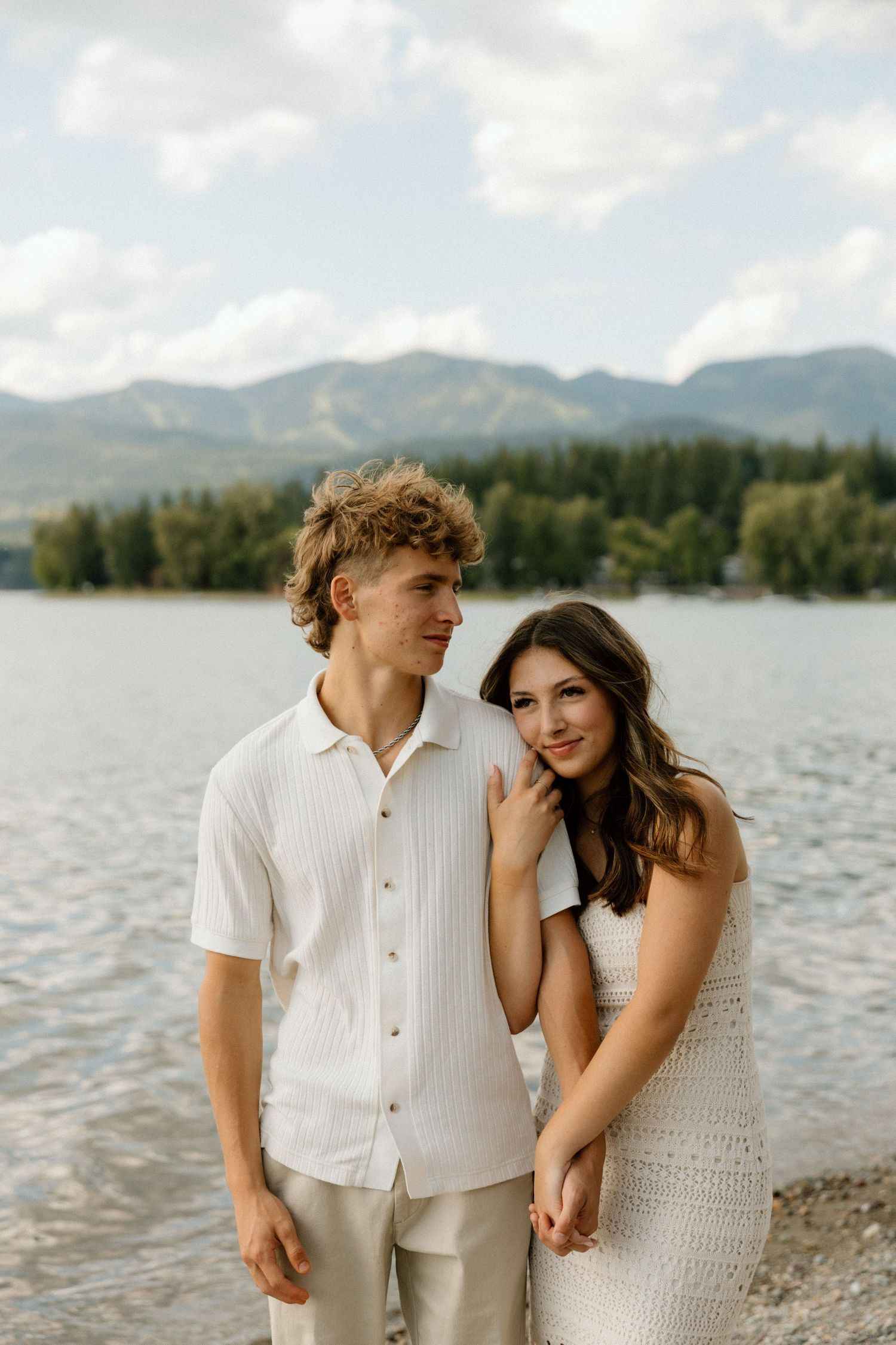 Romantic lakeside photoshoot with mountain backdrop and cloudy skies.