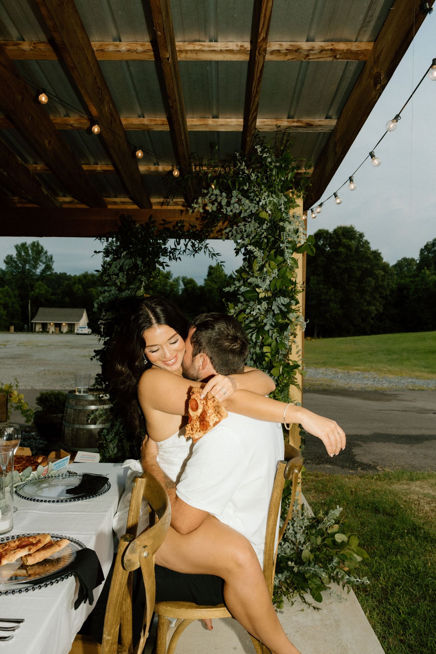 A couple shares a romantic moment under a rustic wooden pavilion.