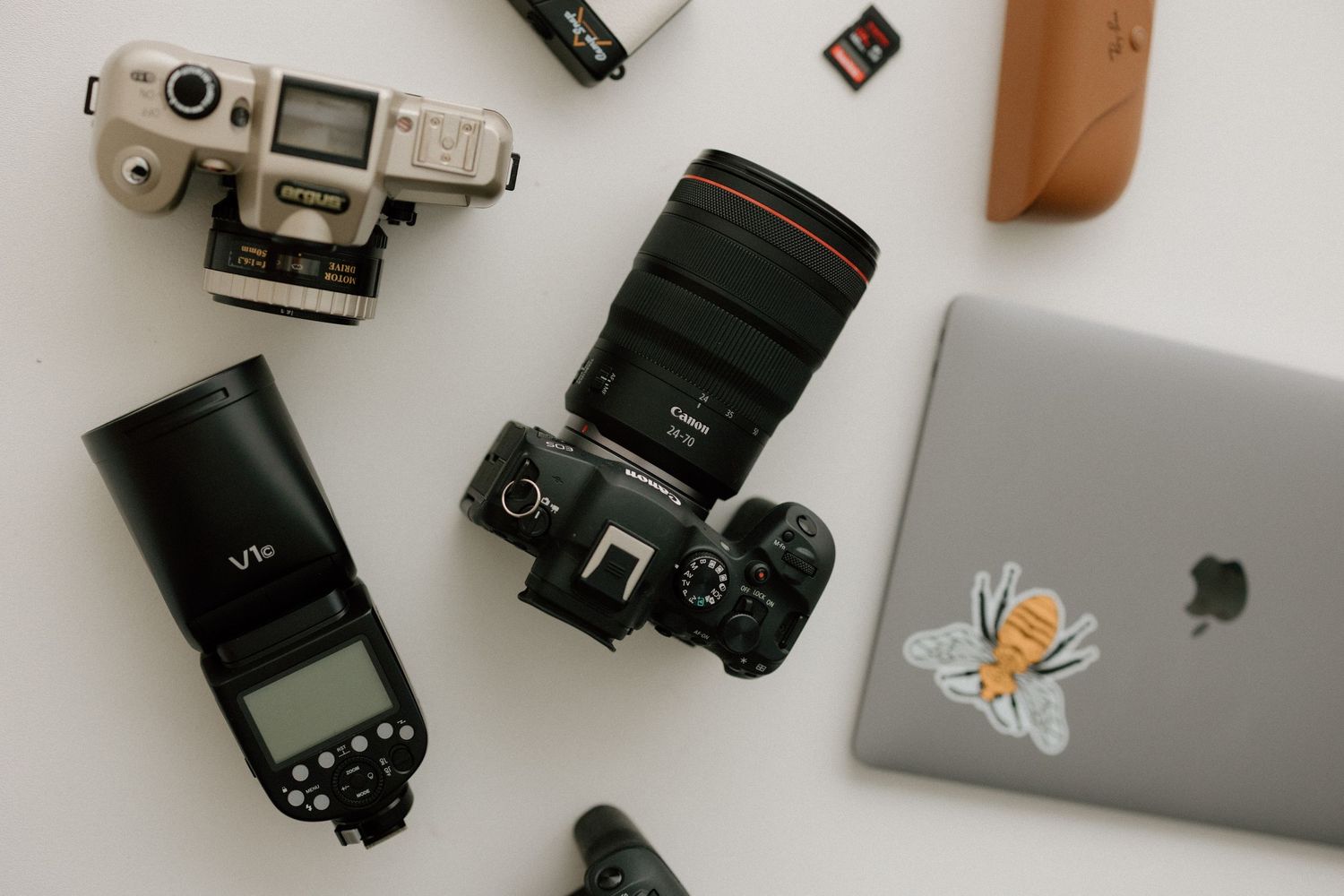 Collection of photography gear including cameras, lenses and laptop arranged on white surface.