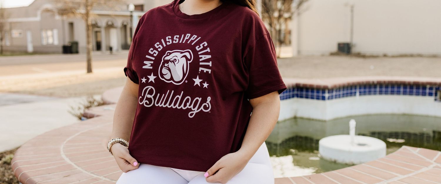 A maroon Bulldogs t-shirt and white pants outfit shown against a neutral wall backdrop.