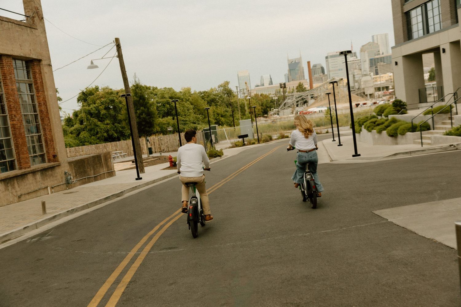 Two cyclists riding down a hill with a city skyline visible in the background.