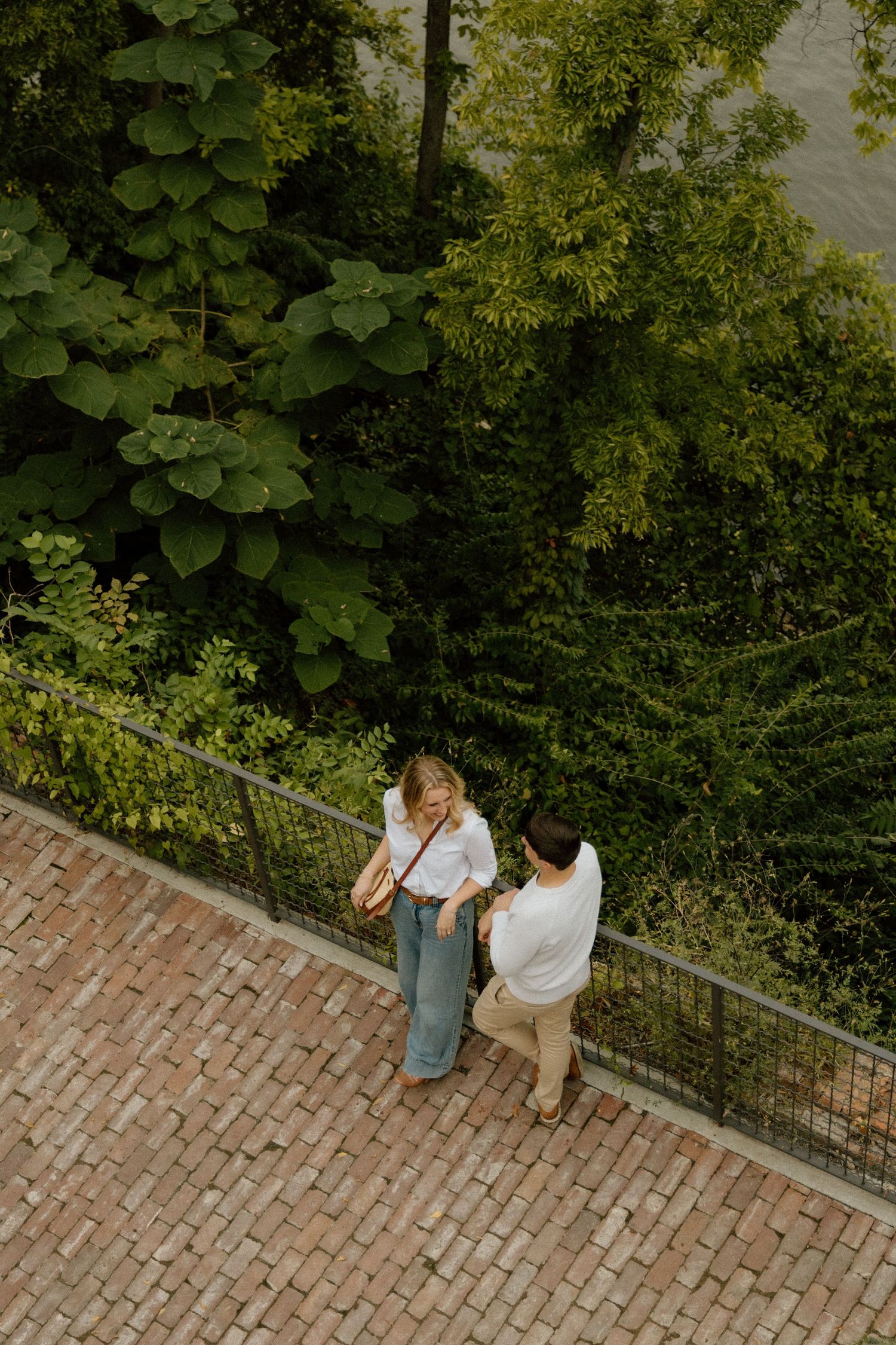 Couple sits intimately on brick steps surrounded by lush greenery.
