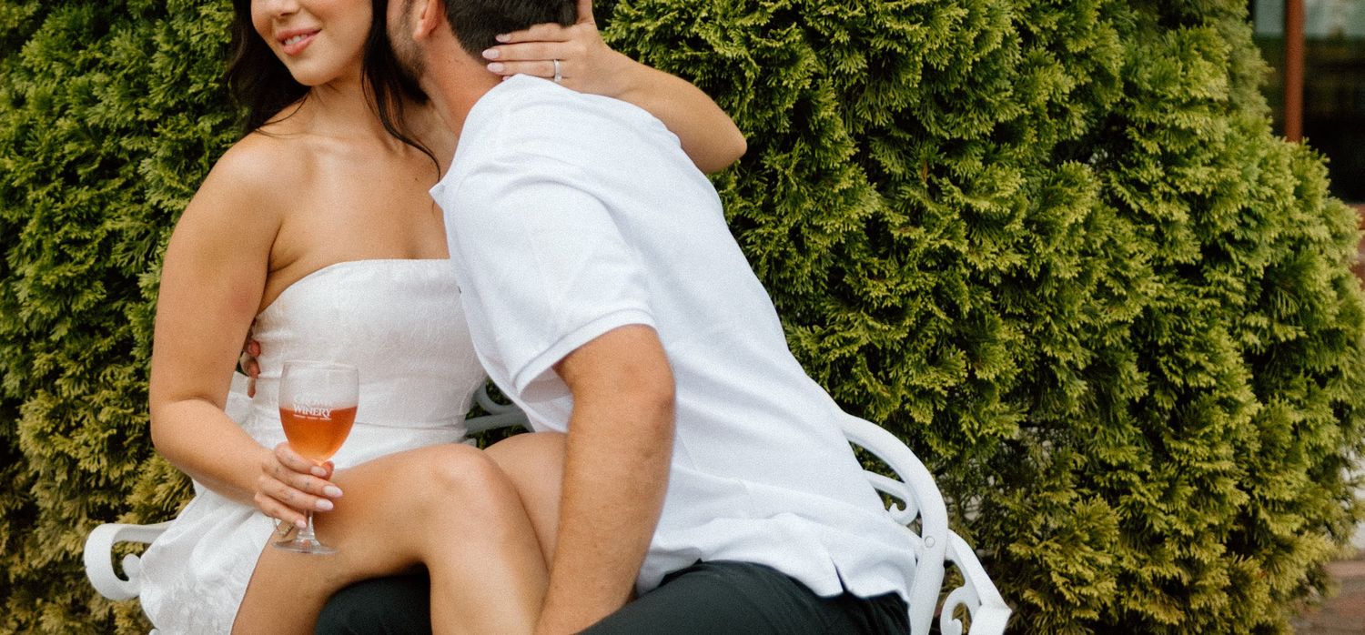 A couple embraces against a backdrop of green hedges in an outdoor setting.