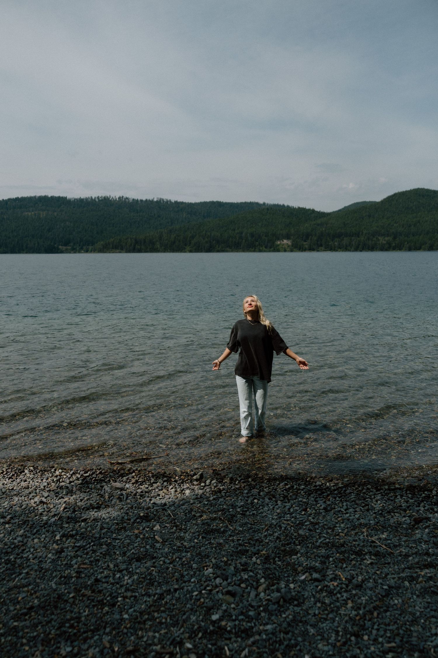 Person standing in lake water with mountains in background.