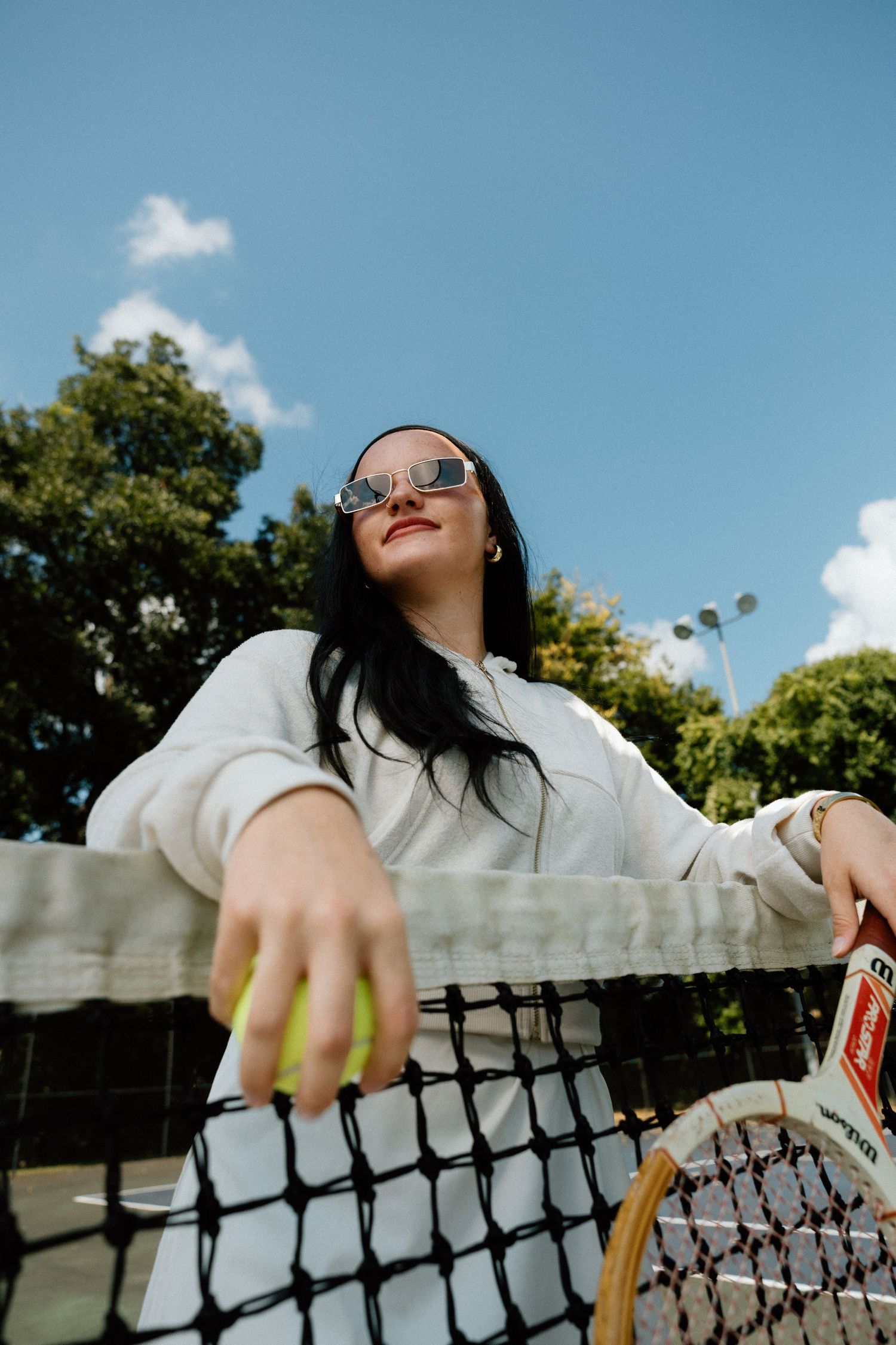 Low angle shot of someone in white clothing leaning against a tennis net outdoors.
