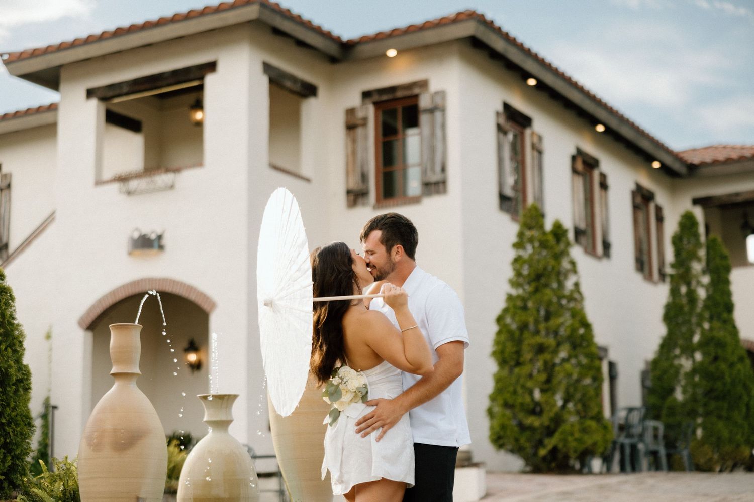 Couple embracing outside Mediterranean-style villa with arched doorway.