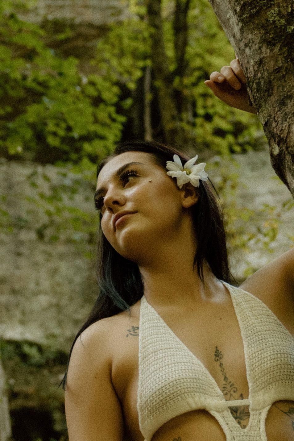 Artistic outdoor portrait series in cream crochet top with flower accessory against forest backdrop.