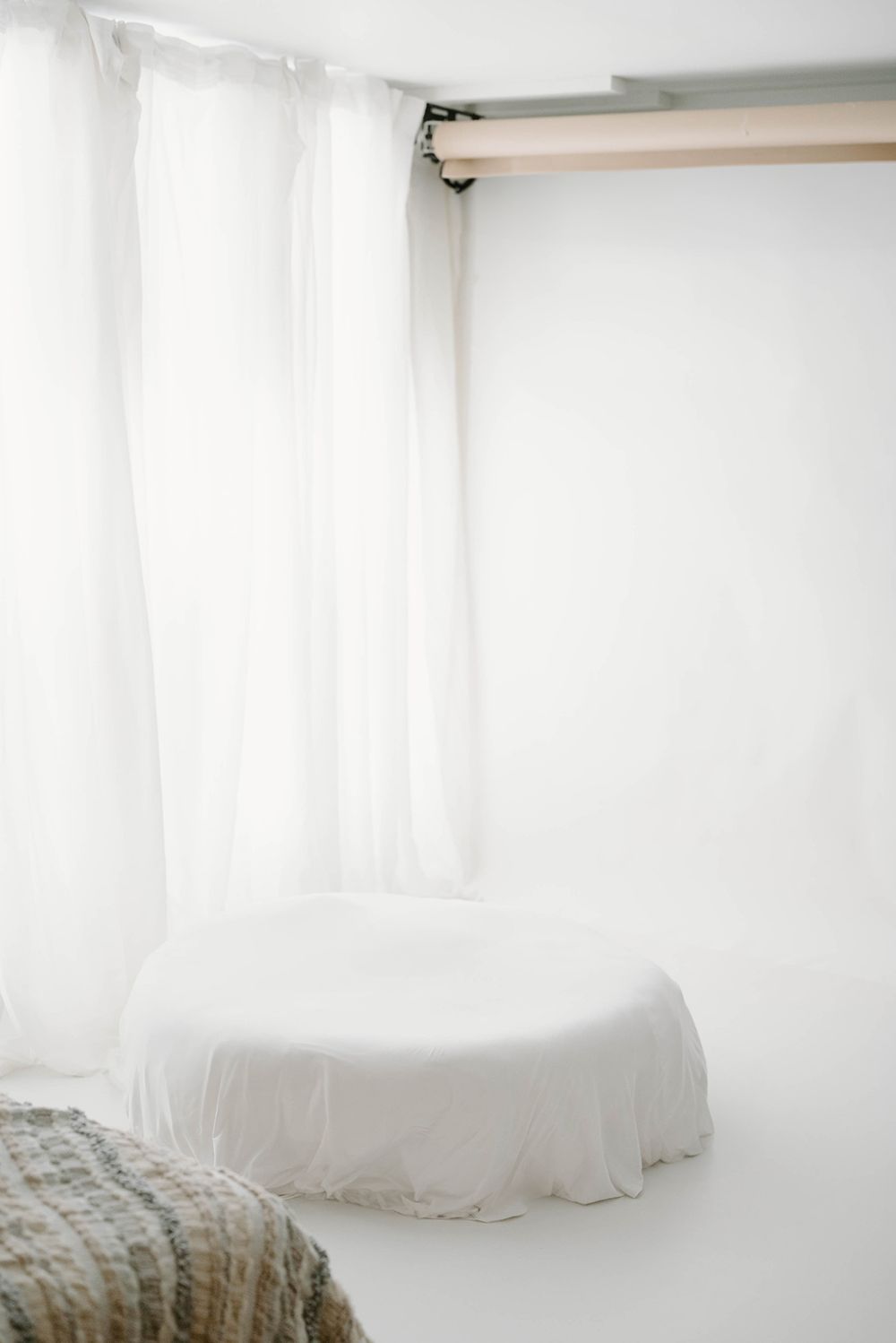 A minimalist white photography studio, in Leduc Alberta with sheer curtains and a round white posing prop.
