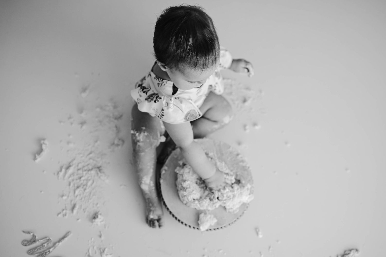 Black and white overhead photo of baby enjoying first birthday cake smash session.