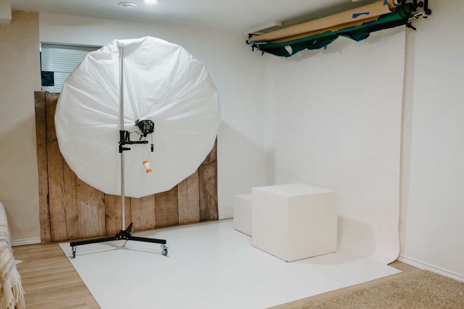 A large white circular photography umbrella light on a stand in a minimalist studio with wooden backdrop.