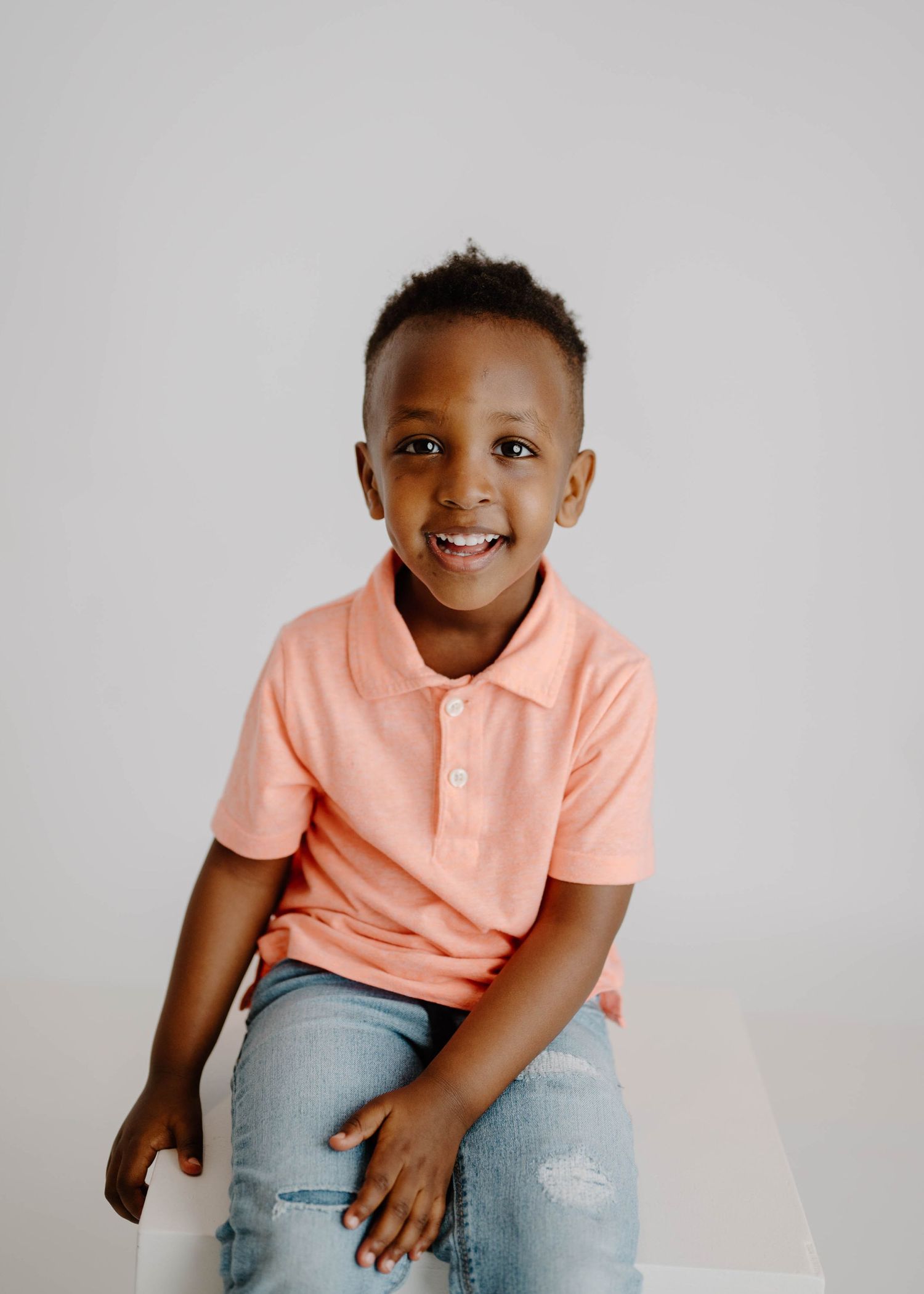 Smiling young boy in coral polo shirt and jeans on white background.
