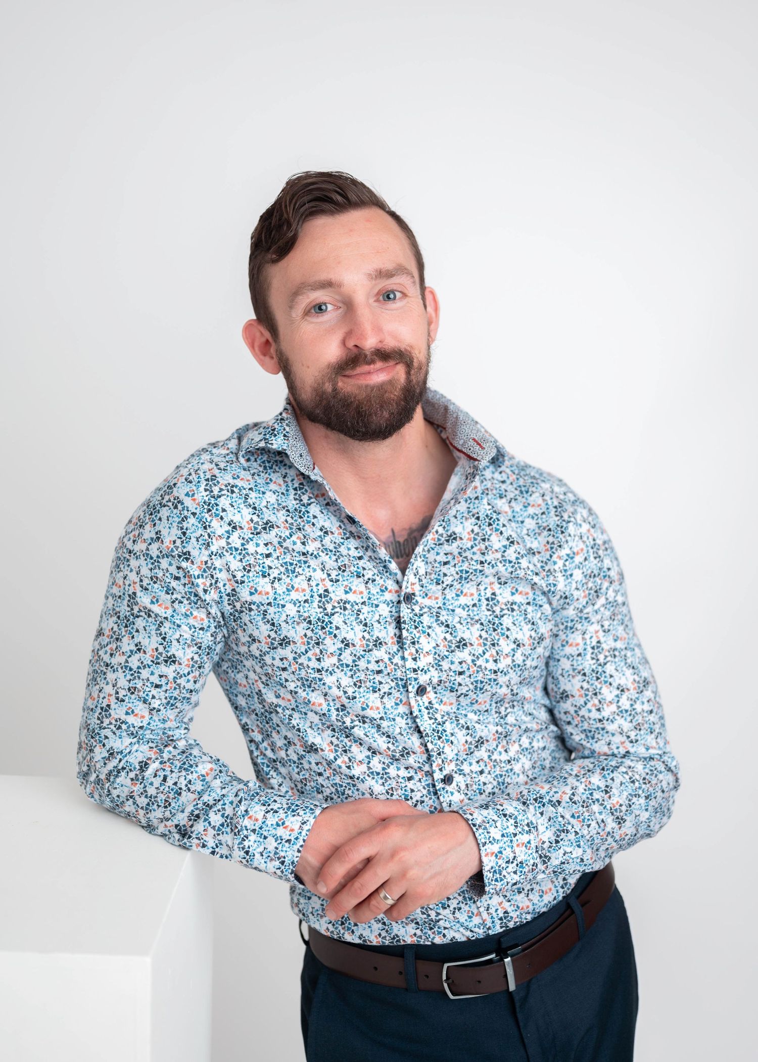 Man in floral blue shirt with beard smiling, posing against white background in professional portrait photo.