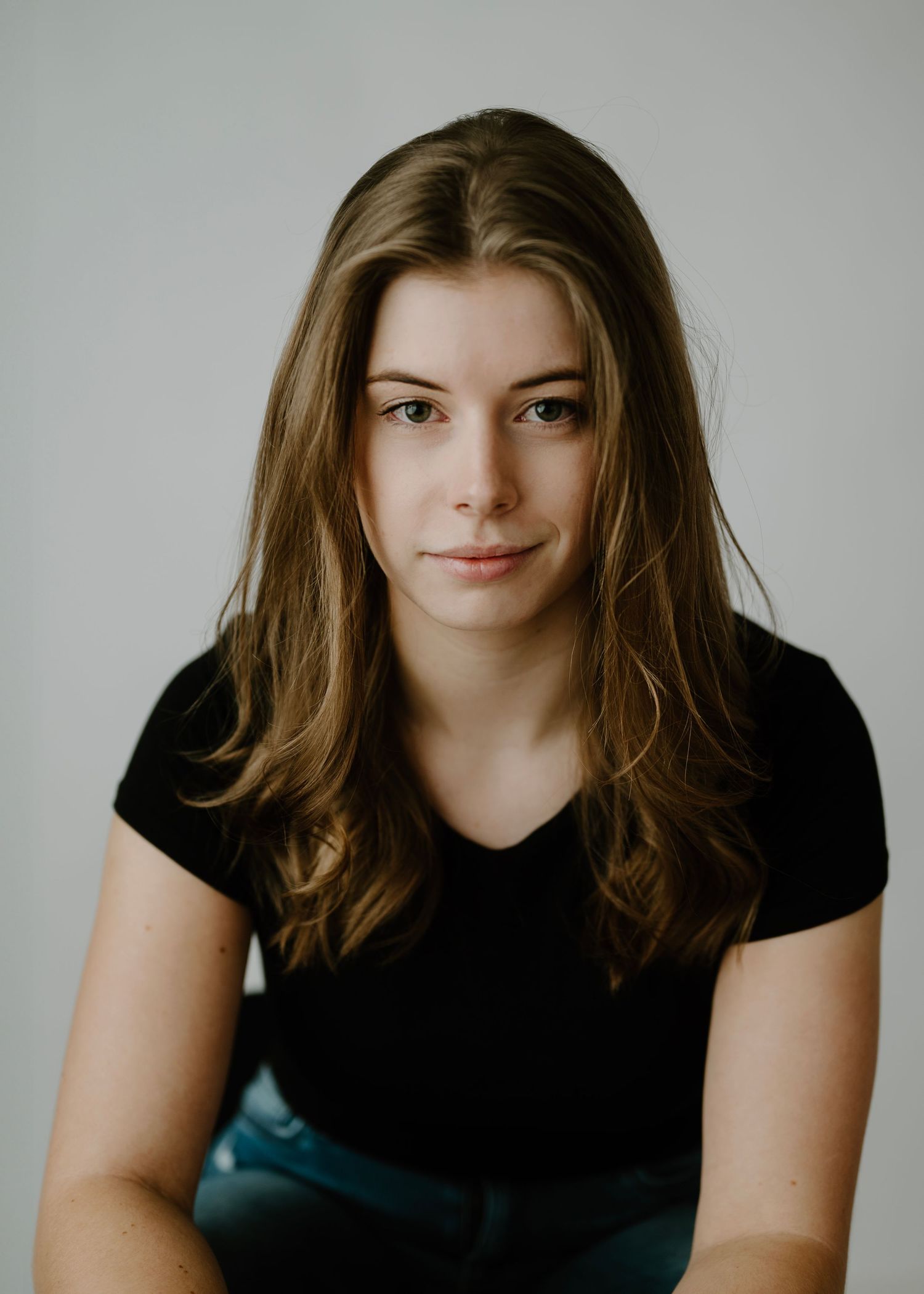 Young brunette woman in black t-shirt with natural expression against light gray studio background.