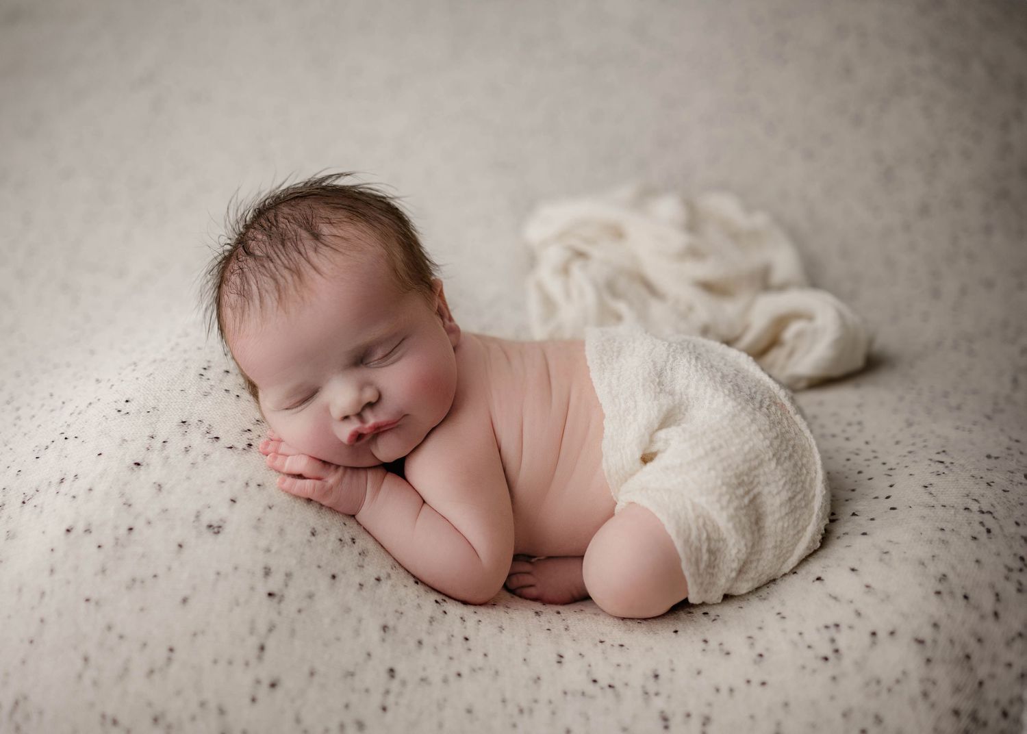 Peaceful newborn baby sleeping curled up on a soft cream blanket in a classic posed newborn photography session.