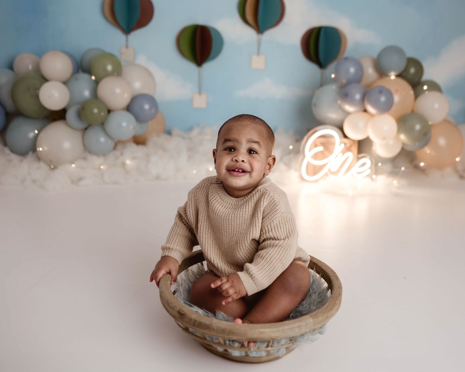 Smiling baby boy sitting in a decorative bowl at a hot air balloon themed first birthday cake smash photo session.