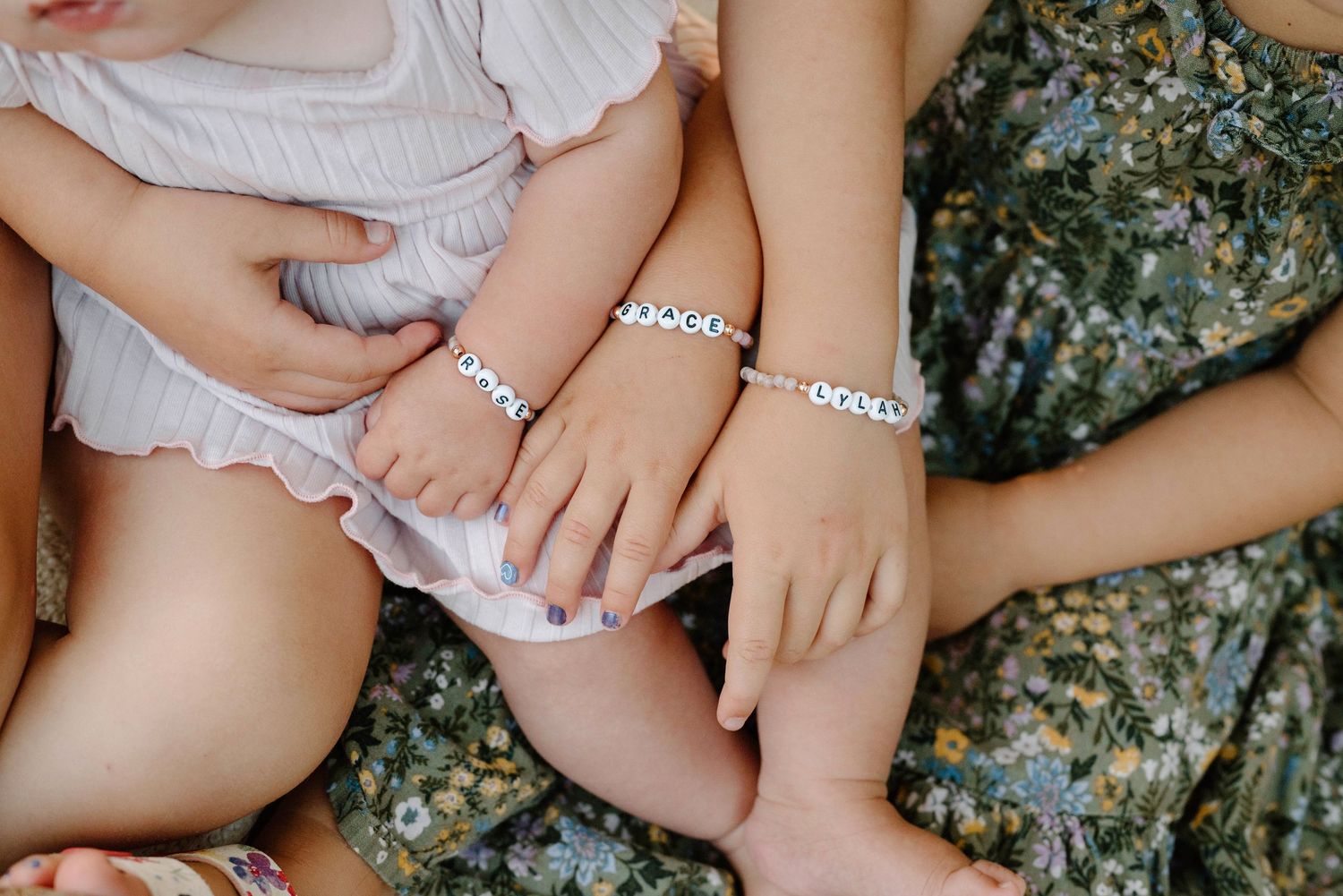 Close-up of three young sisters wearing matching silver charm bracelets on their tiny wrists.