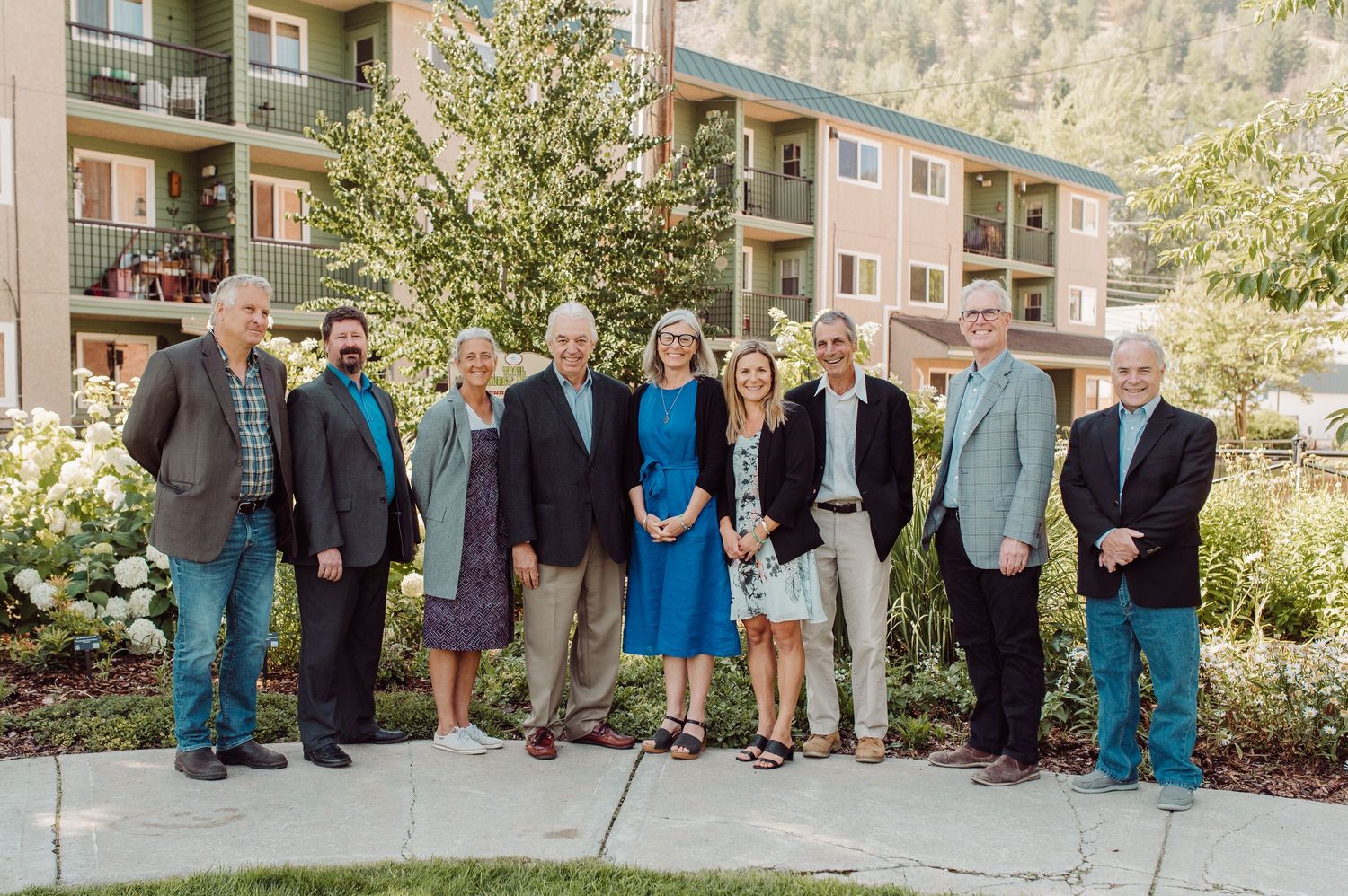 Group of ten professionals posing outdoors in front of a modern apartment building complex.