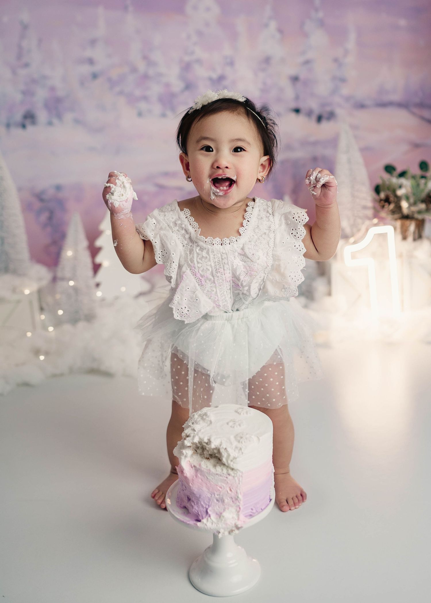 Excited baby girl smashing white cake at winter wonderland themed first birthday photo session.