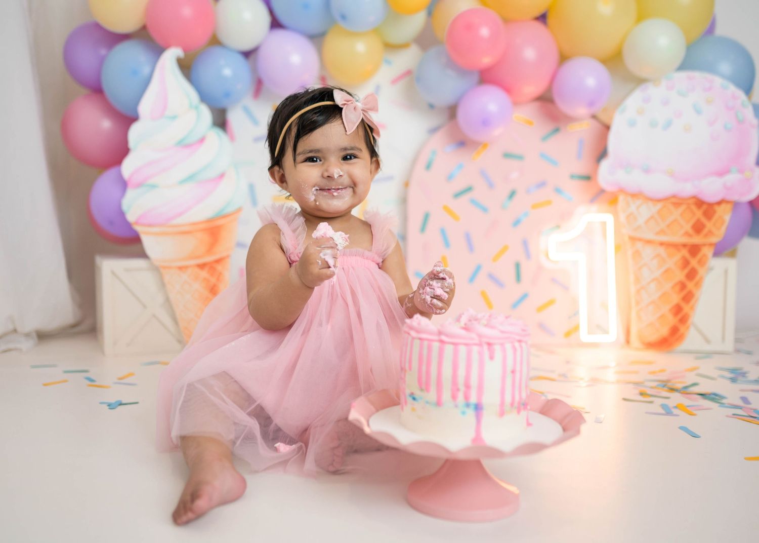 A baby girl in a pink tutu dress celebrates her first birthday with a cake smash in an ice cream themed photo session.