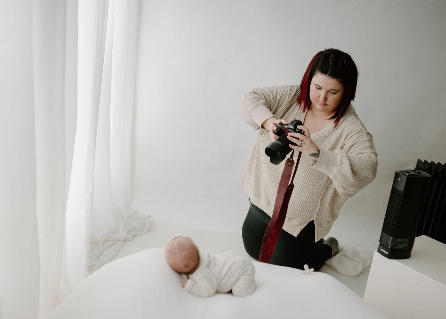Female photographer capturing a newborn baby lying on a white surface in a bright studio.