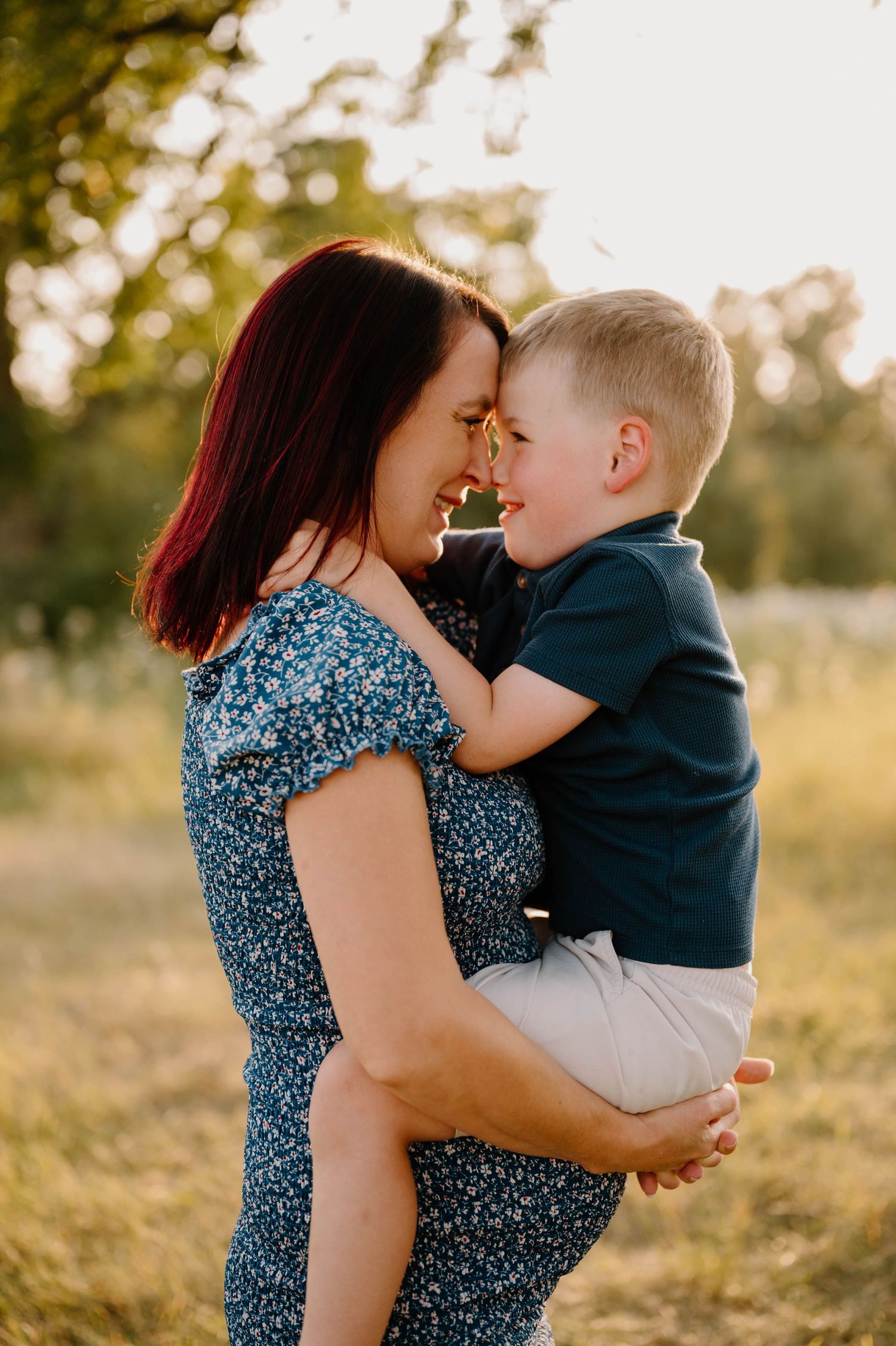 Loving mother holding smiling toddler son face-to-face in sunny green park at golden hour.