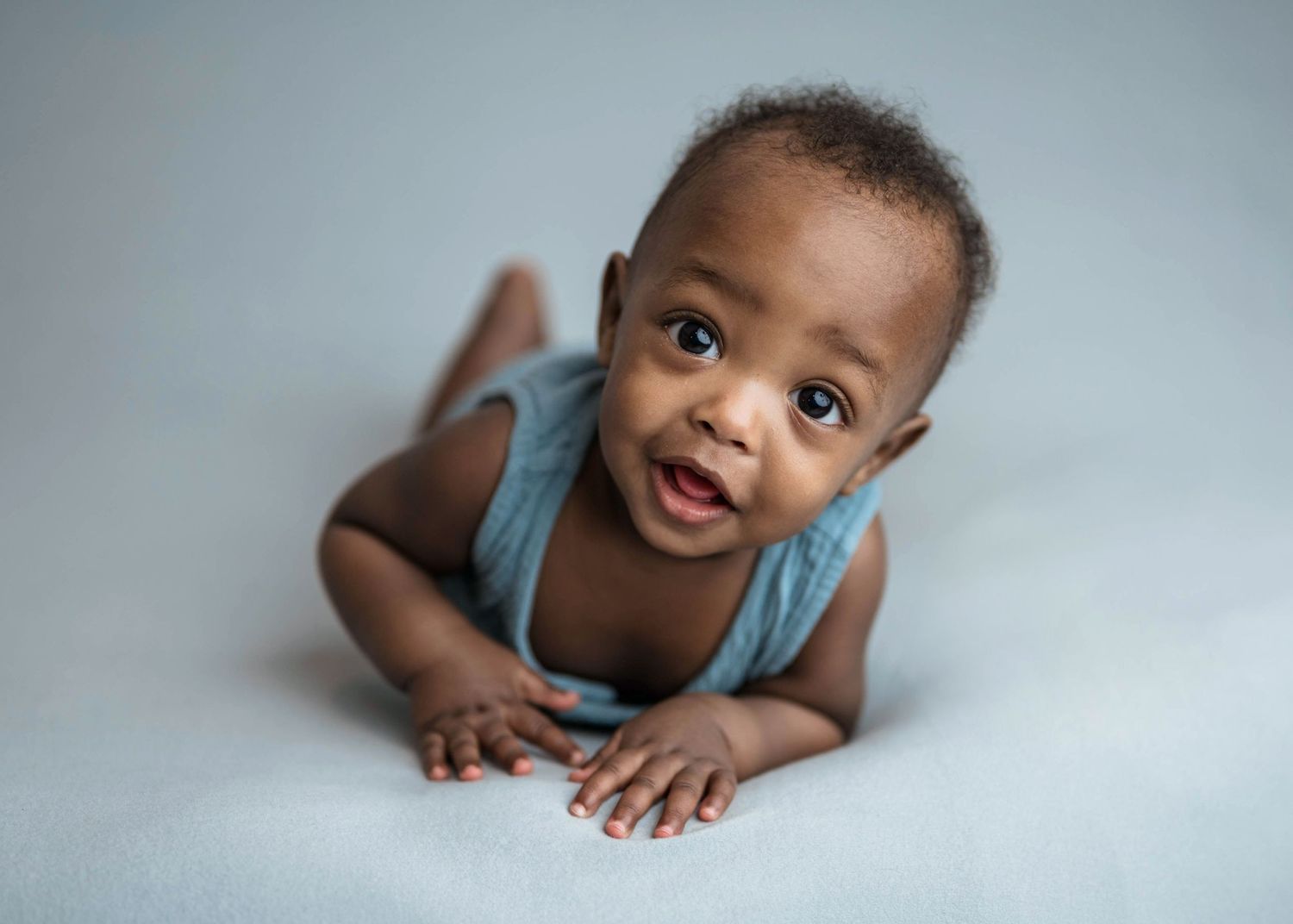 Cute baby in blue wrap doing tummy time on gray background.