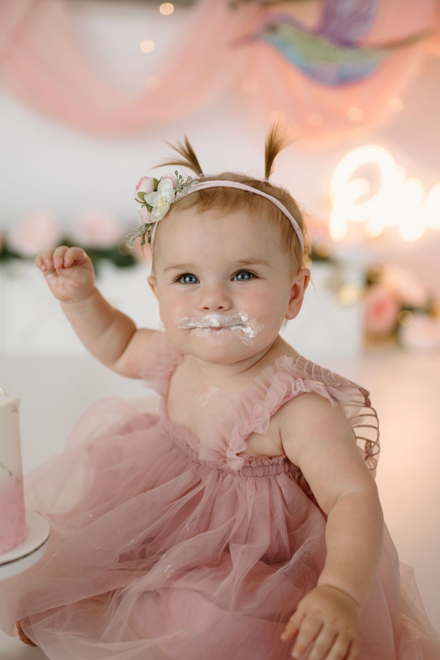 Baby girl in pink tulle dress with cake on her face during first birthday cake smash photo session.