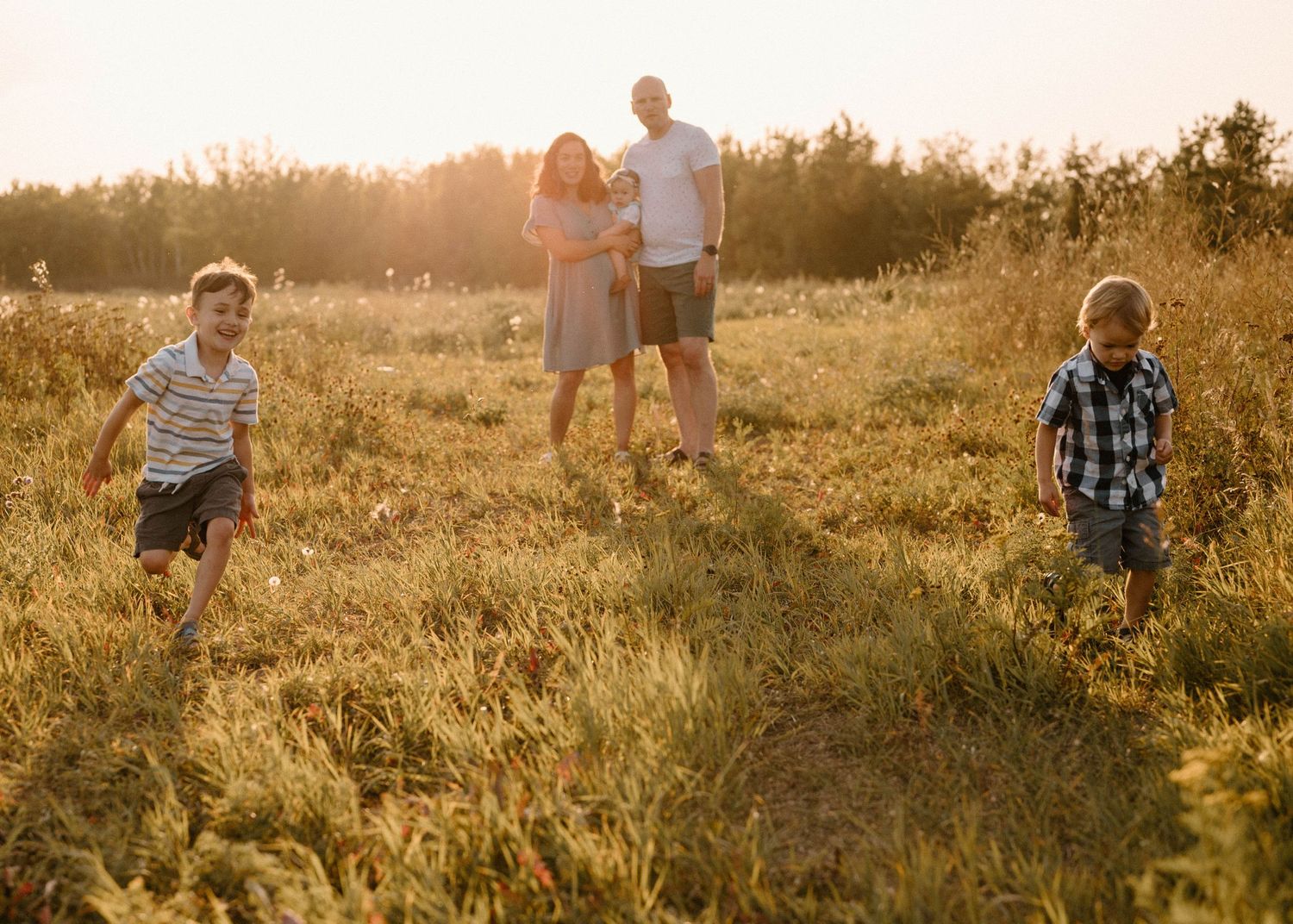 Parents watch their two energetic boys run through a sun-drenched meadow during a family portrait session.