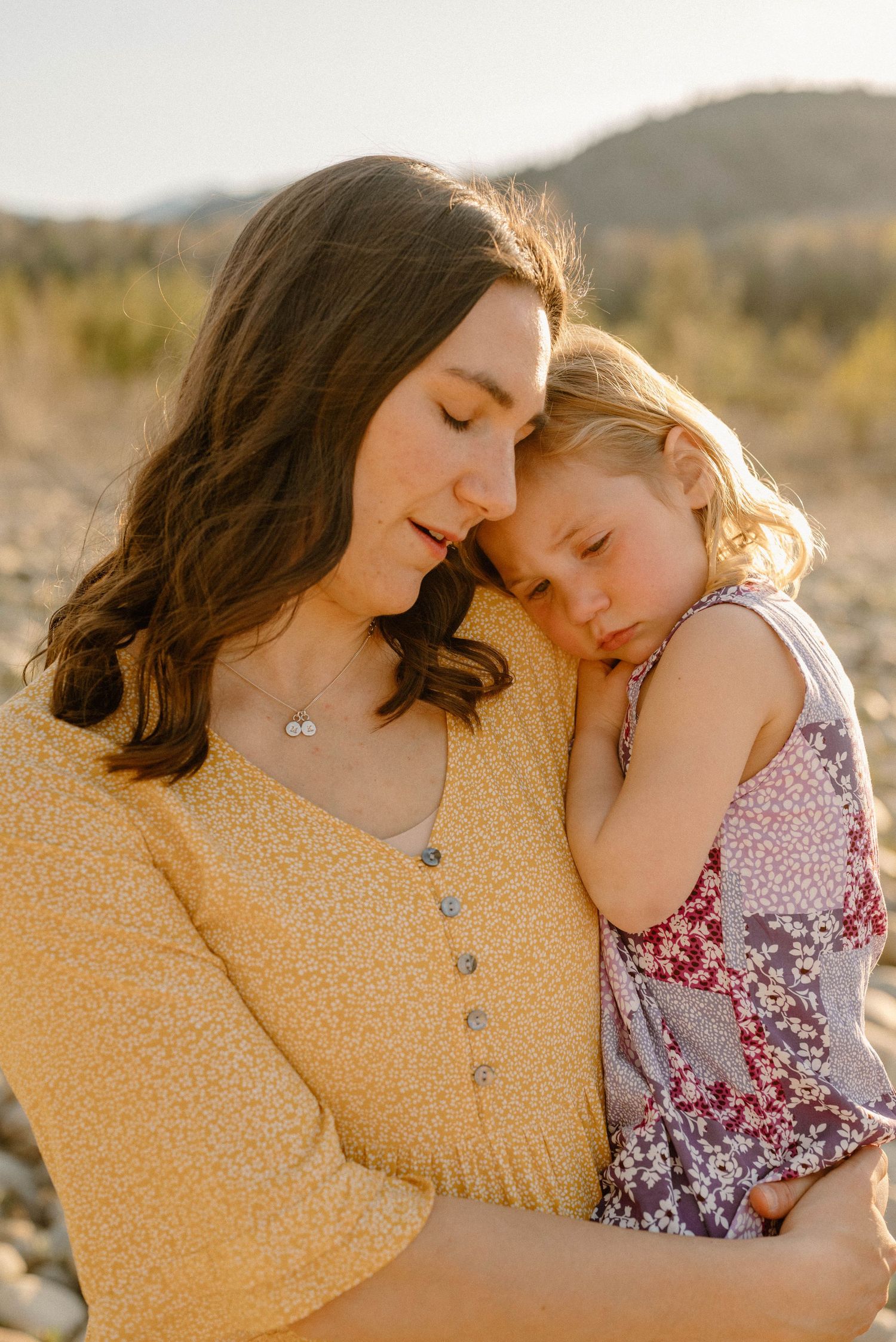 Tender moment of a mother in yellow dress holding her young daughter close outdoors.