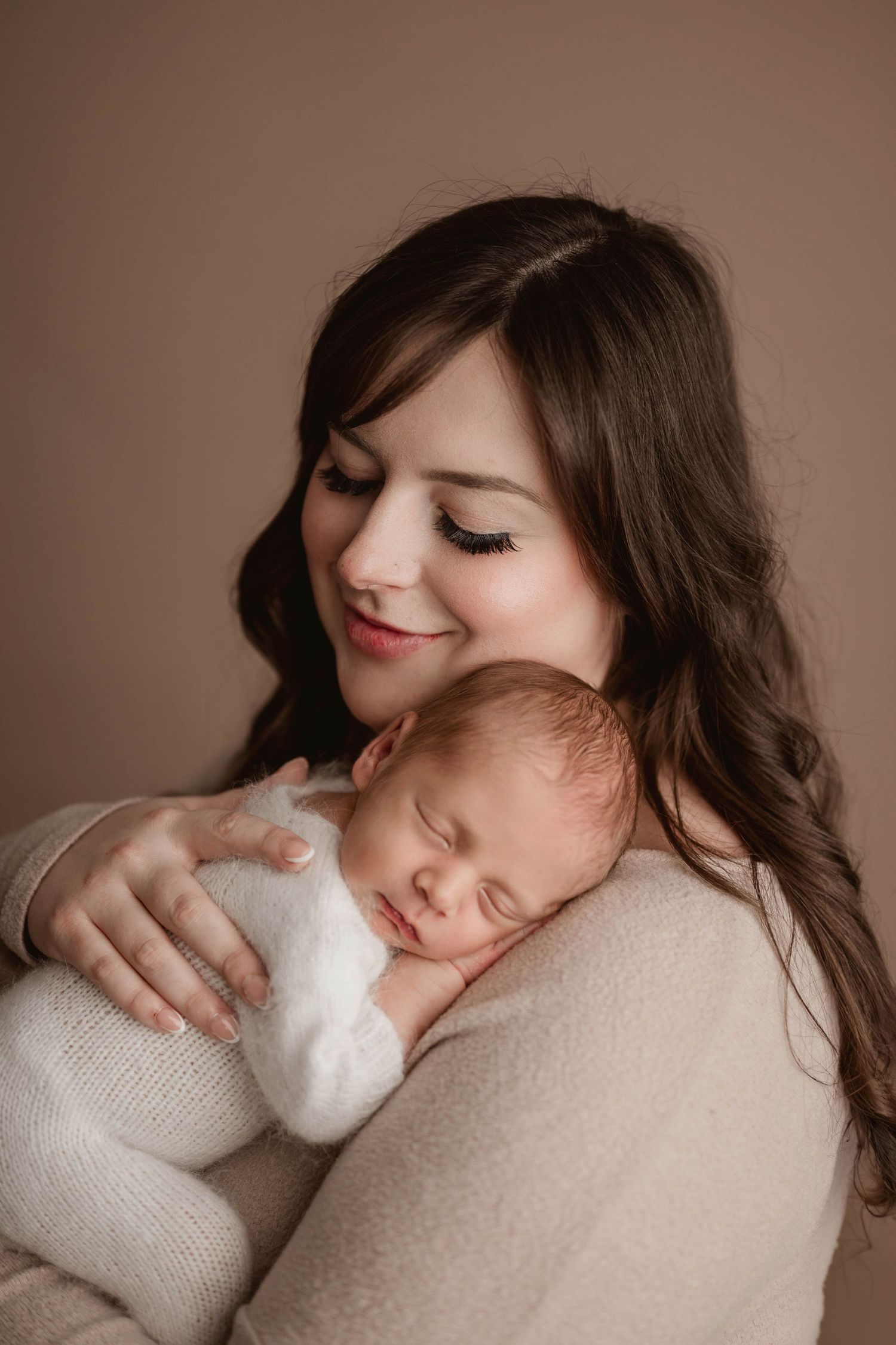 Beautiful mother smiling down at her sleeping newborn baby resting on her shoulder in Cozy Leduc Studio.