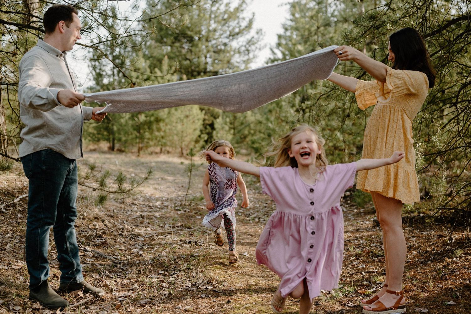 Joyful family playing with a blanket outdoors in a forest setting with laughing children.