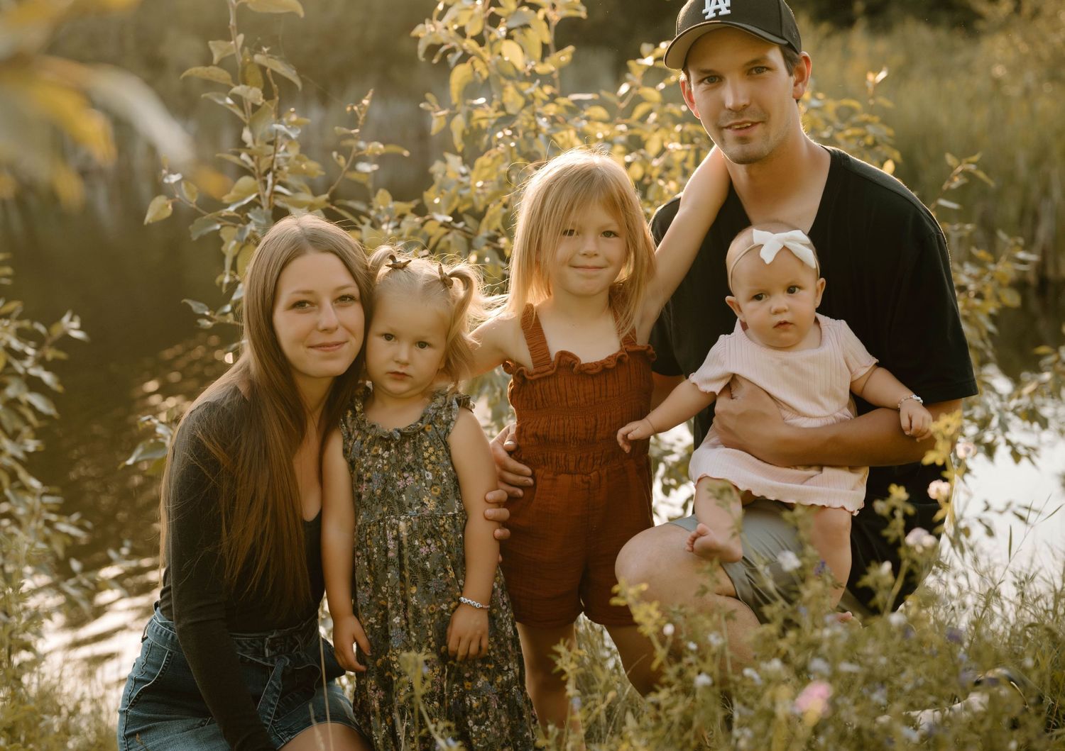Family of five posing together among lush green foliage in warm golden sunset light.