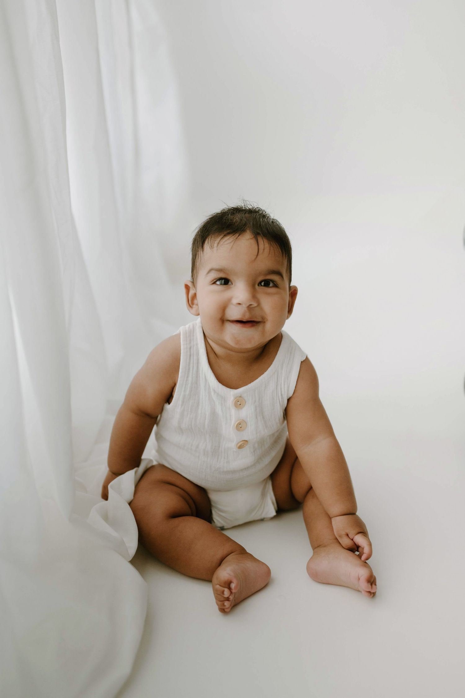 Happy baby in white sleeveless romper smiling on white background.