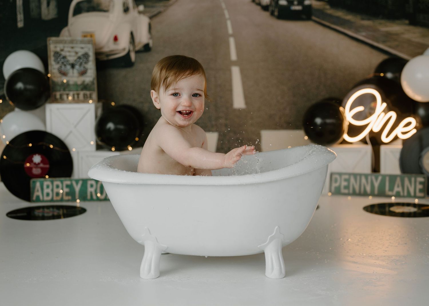 Smiling baby sitting in a white clawfoot bathtub with Beatles Abbey Road birthday party decorations.