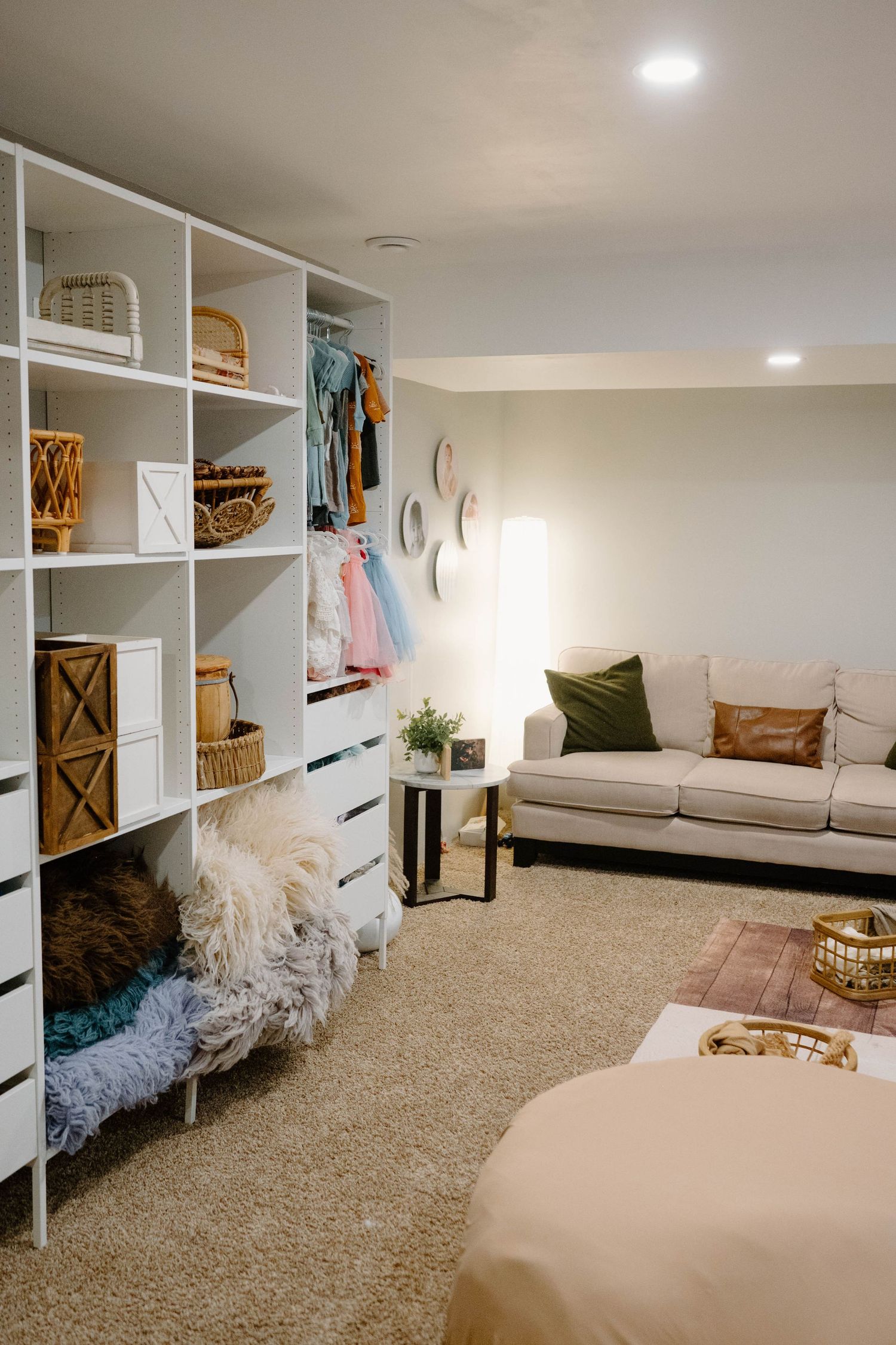 Boho-style Leduc photography studio with white shelving unit, props, cozy sofa, and neutral carpet flooring.