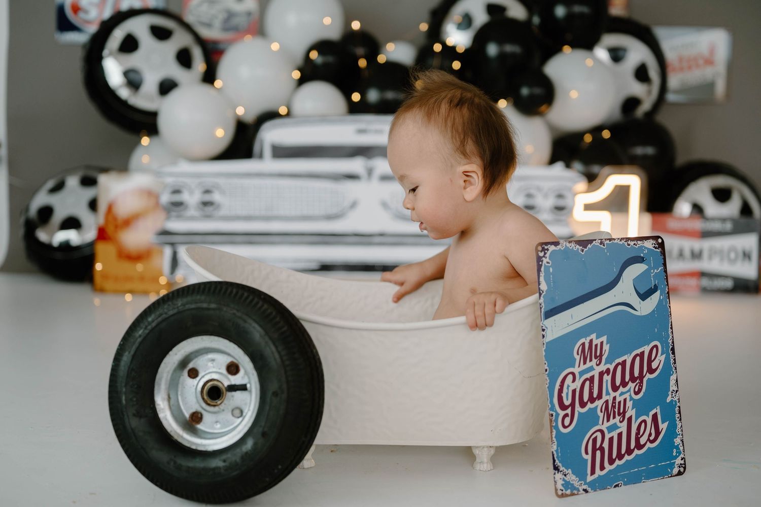 Baby boy sits in miniature bathtub wheel prop at garage-themed first birthday photoshoot.