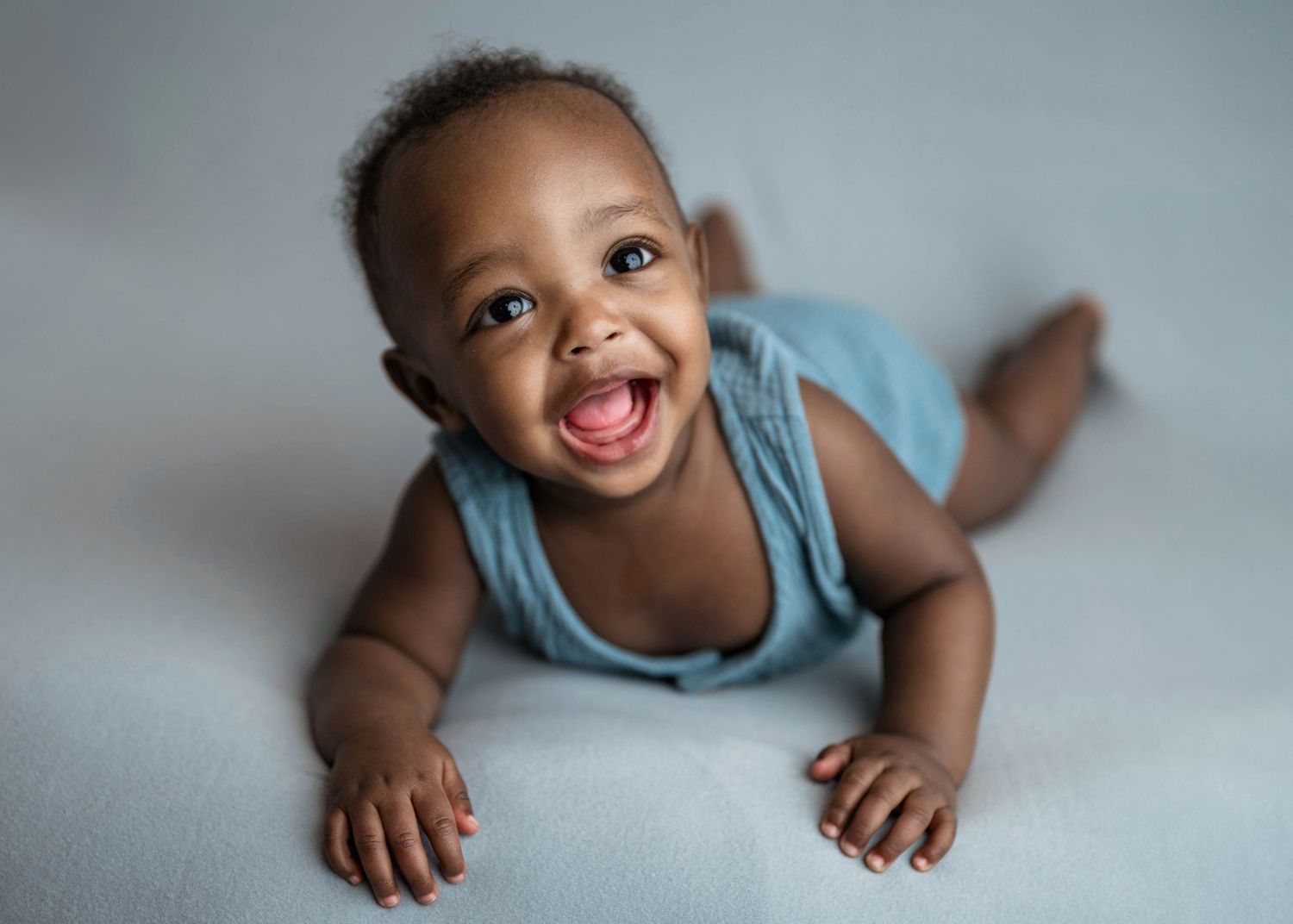Happy baby in blue romper doing tummy time smiling at camera.