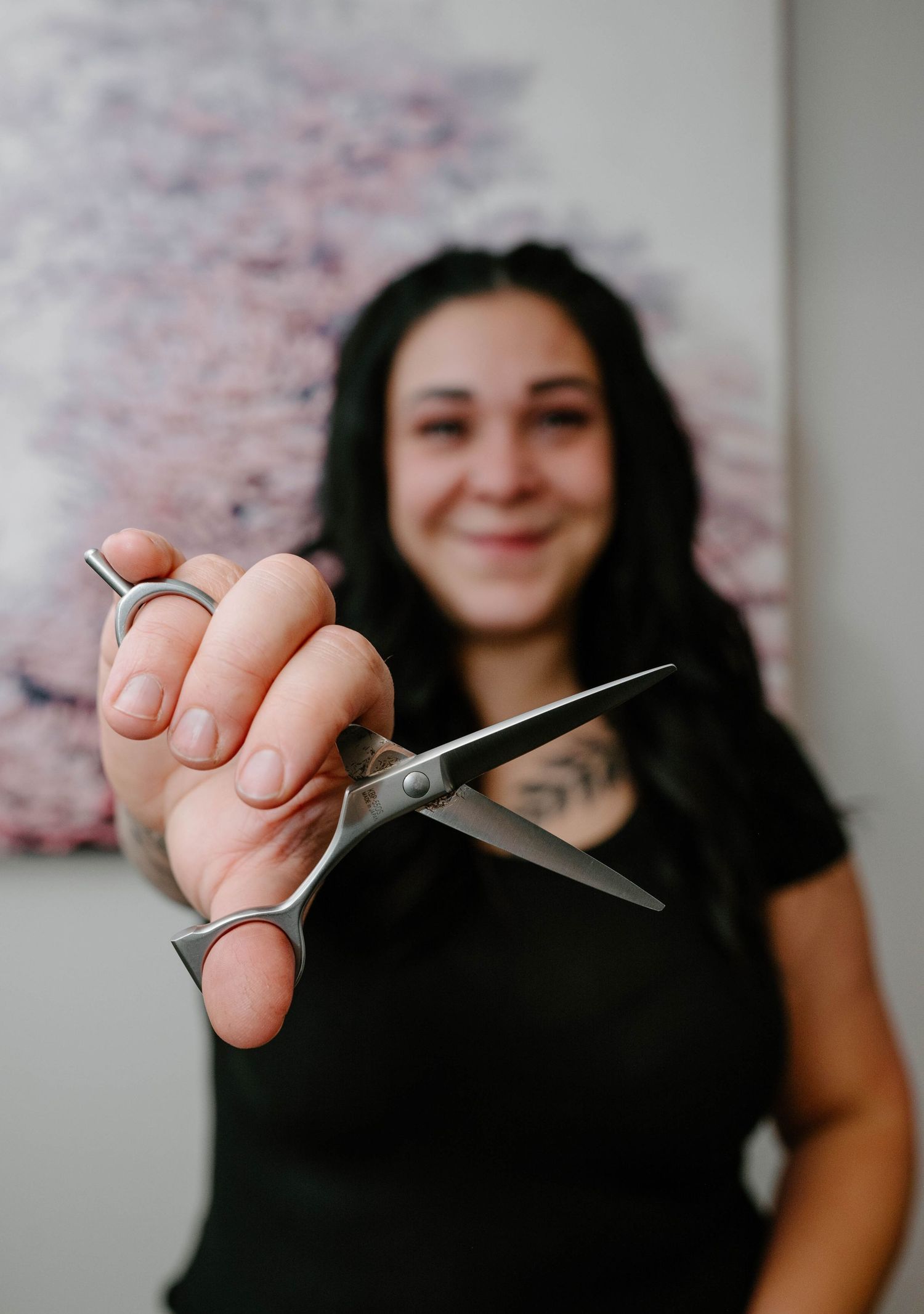 Smiling female hairstylist holding professional hair cutting scissors toward camera in salon for a Branding photoshoot in Leduc.