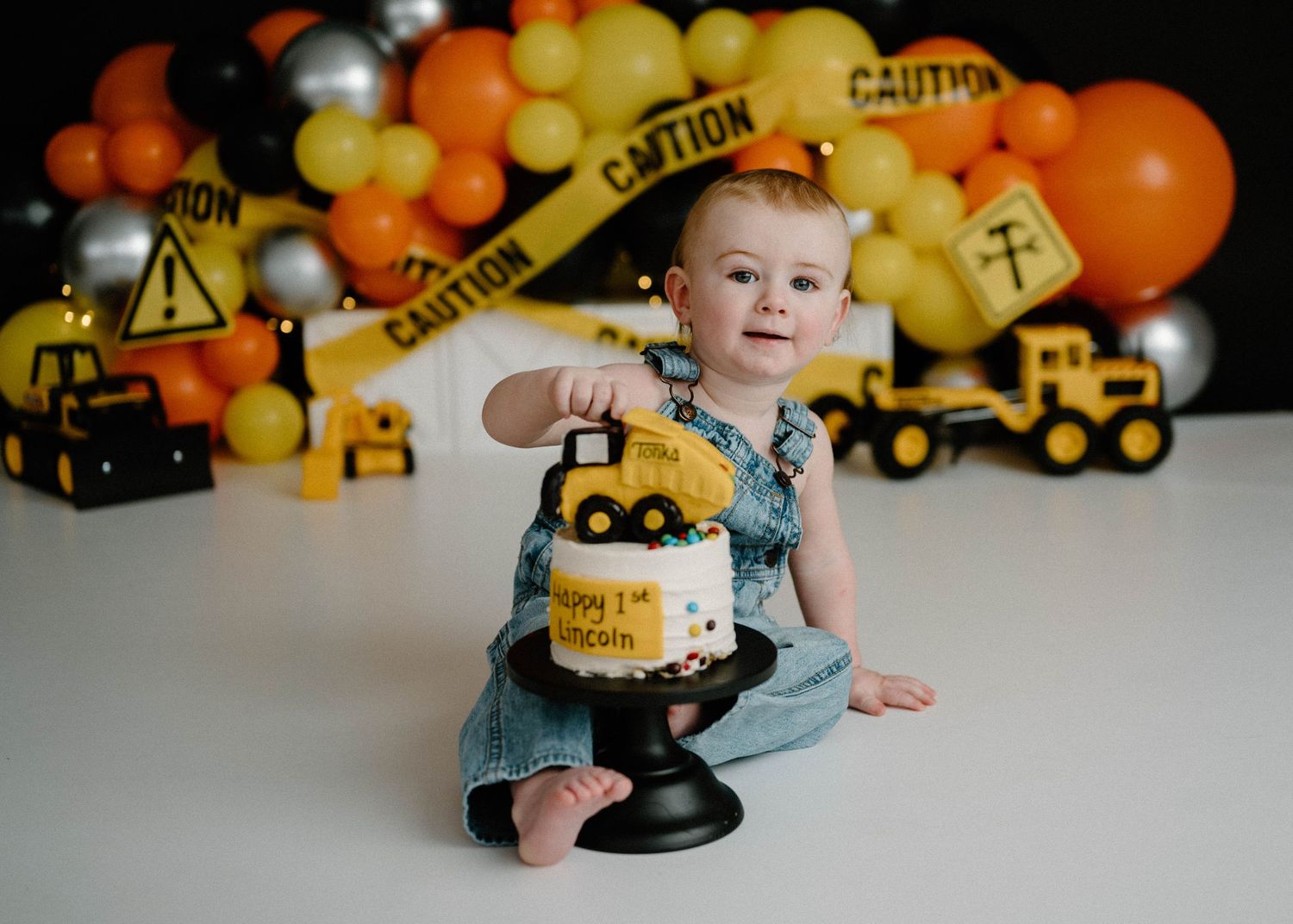 Baby boy at construction themed first birthday cake smash with yellow trucks and caution tape.