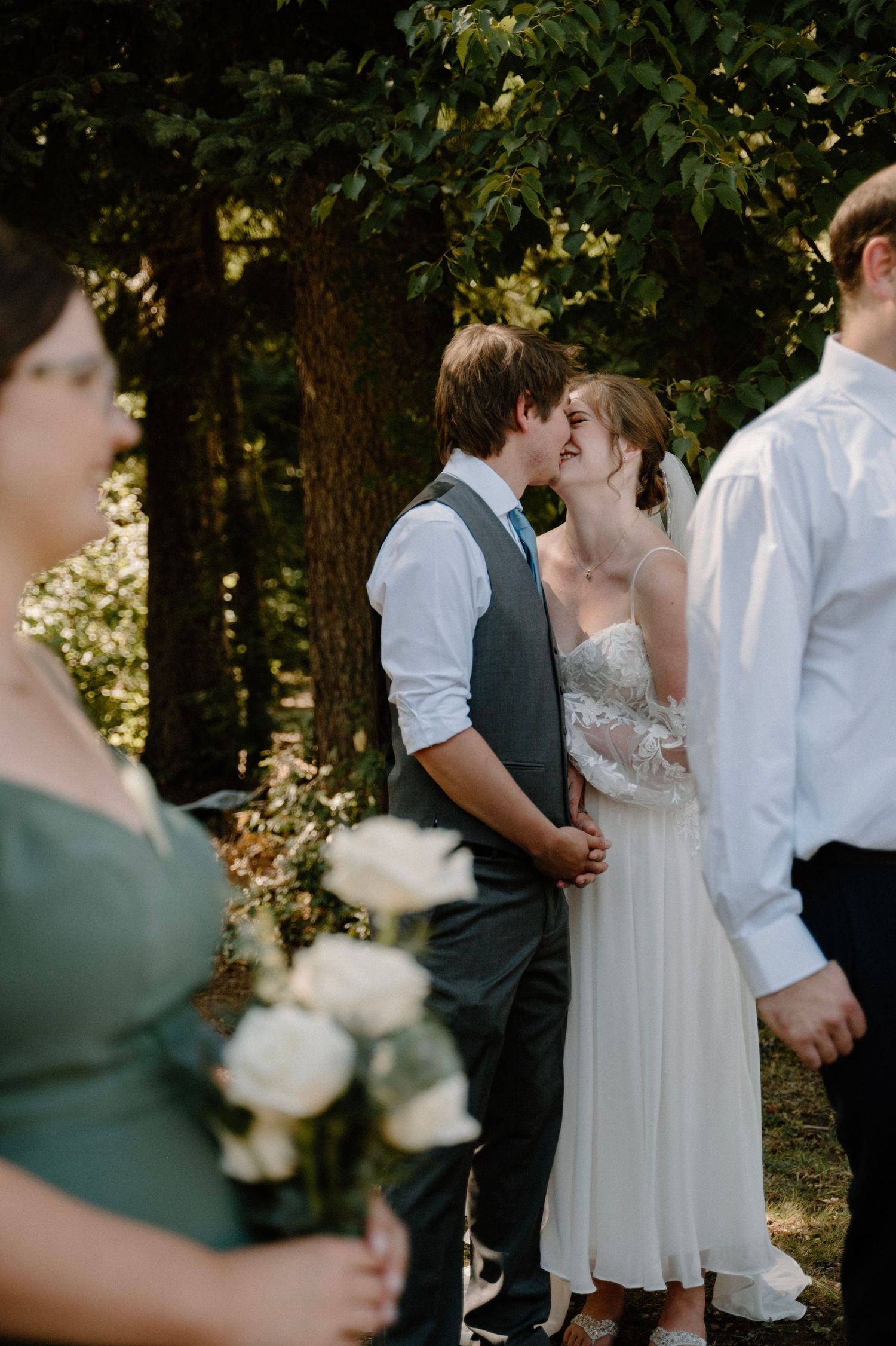 Bride and groom share an intimate kiss during outdoor woodland wedding ceremony at golden hour.
