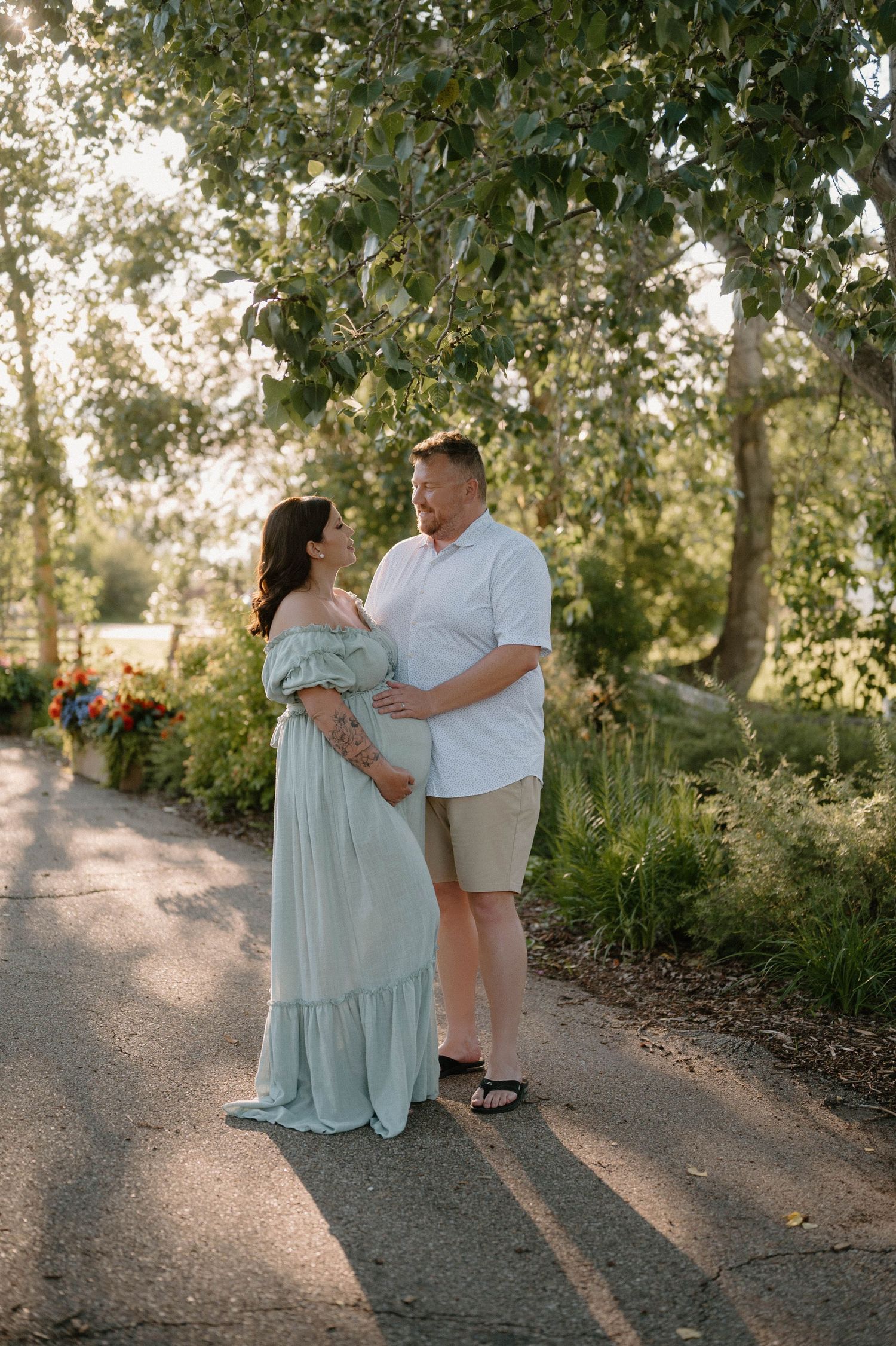 Couple embracing on a garden path, woman in mint maxi dress, man in white shirt, surrounded by lush greenery.