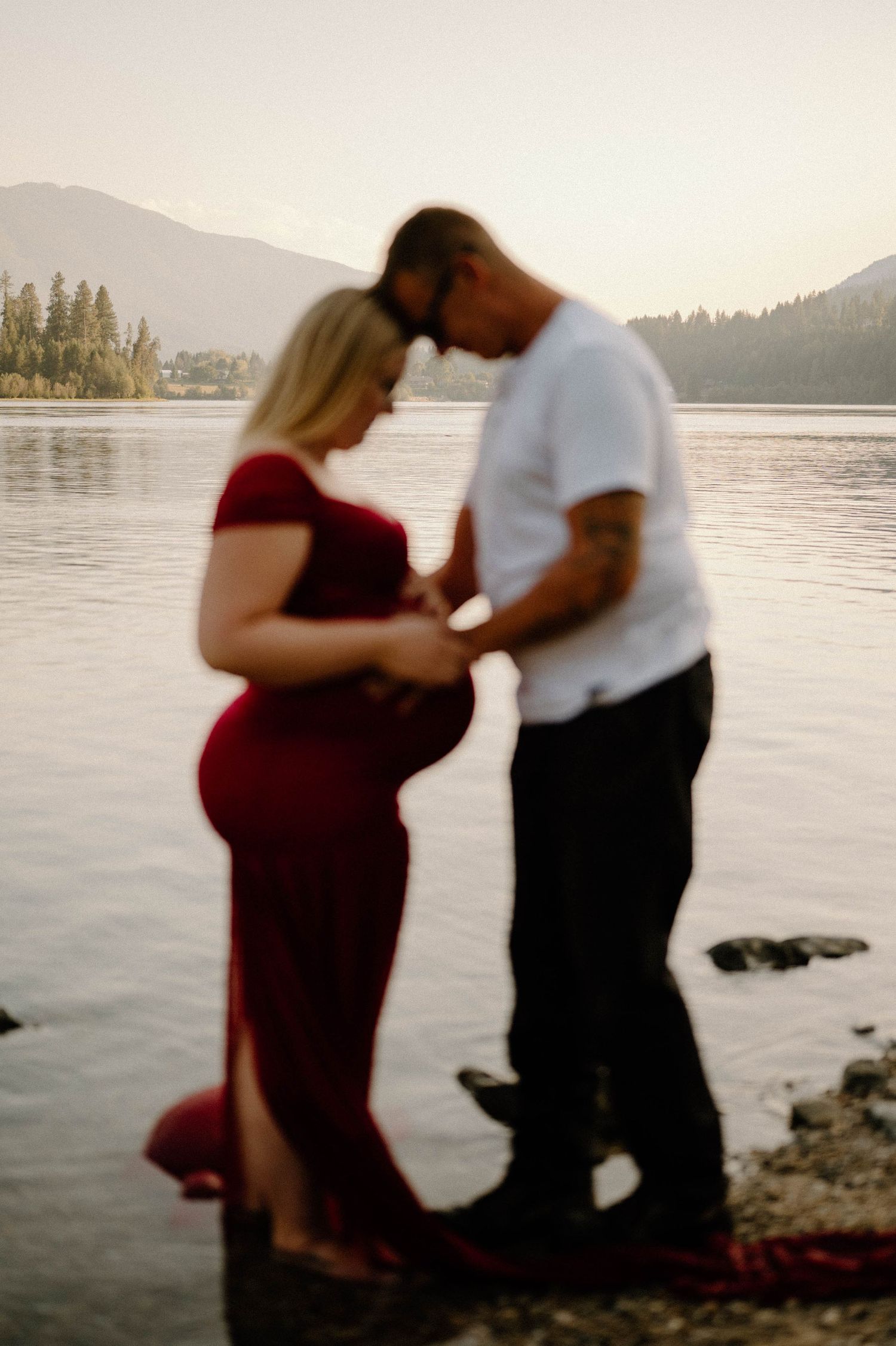 Silhouetted expecting couple holding baby bump together at sunset lakeside.