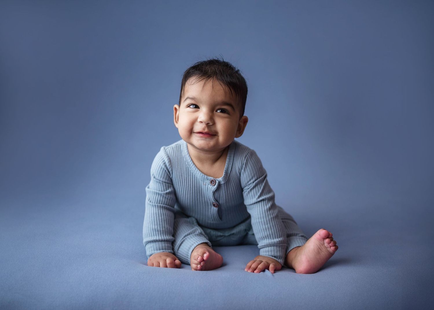 Happy baby boy in blue outfit crawling and smiling on blue backdrop.