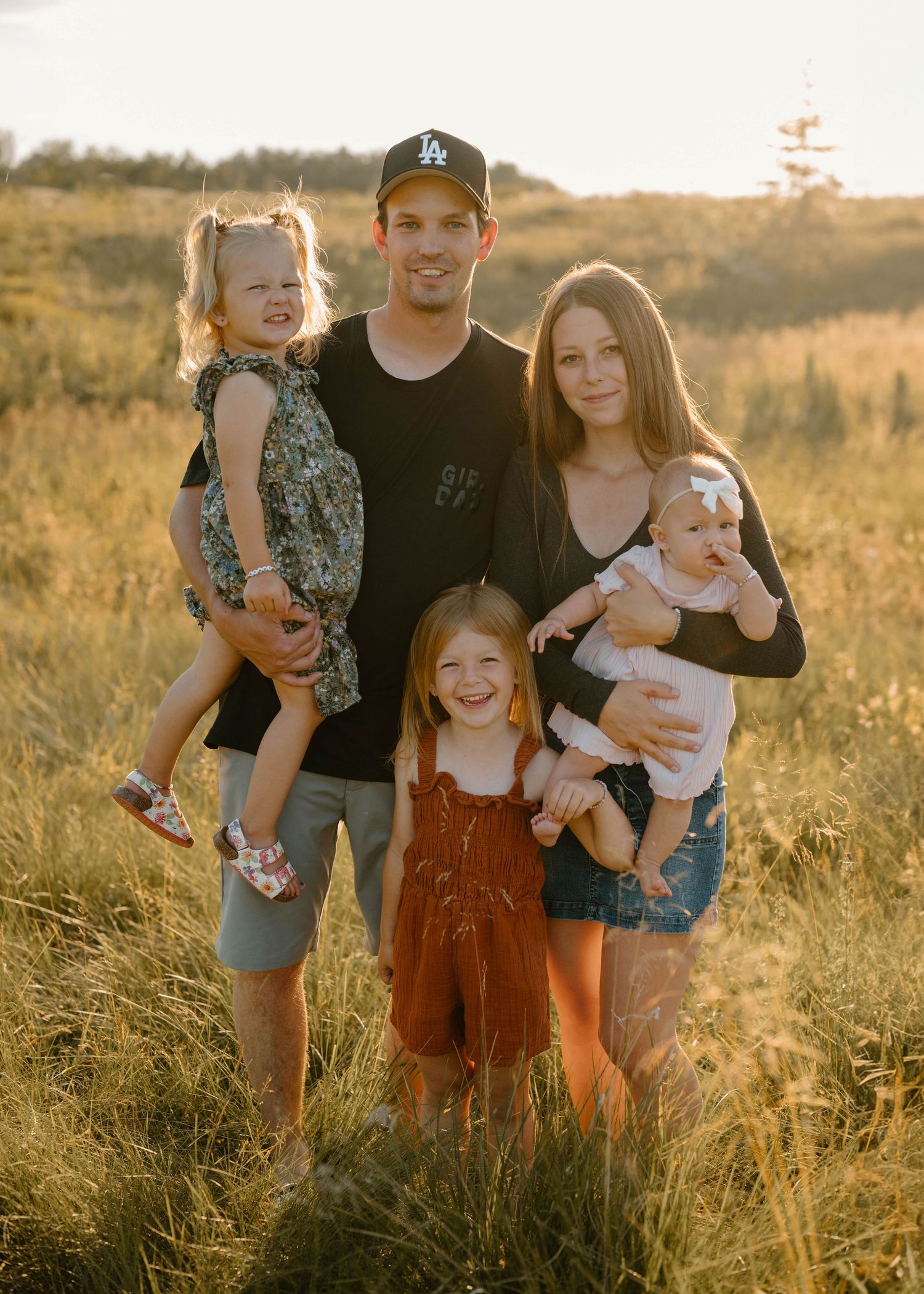Family of five posing together in a sunlit golden grass field at sunset.