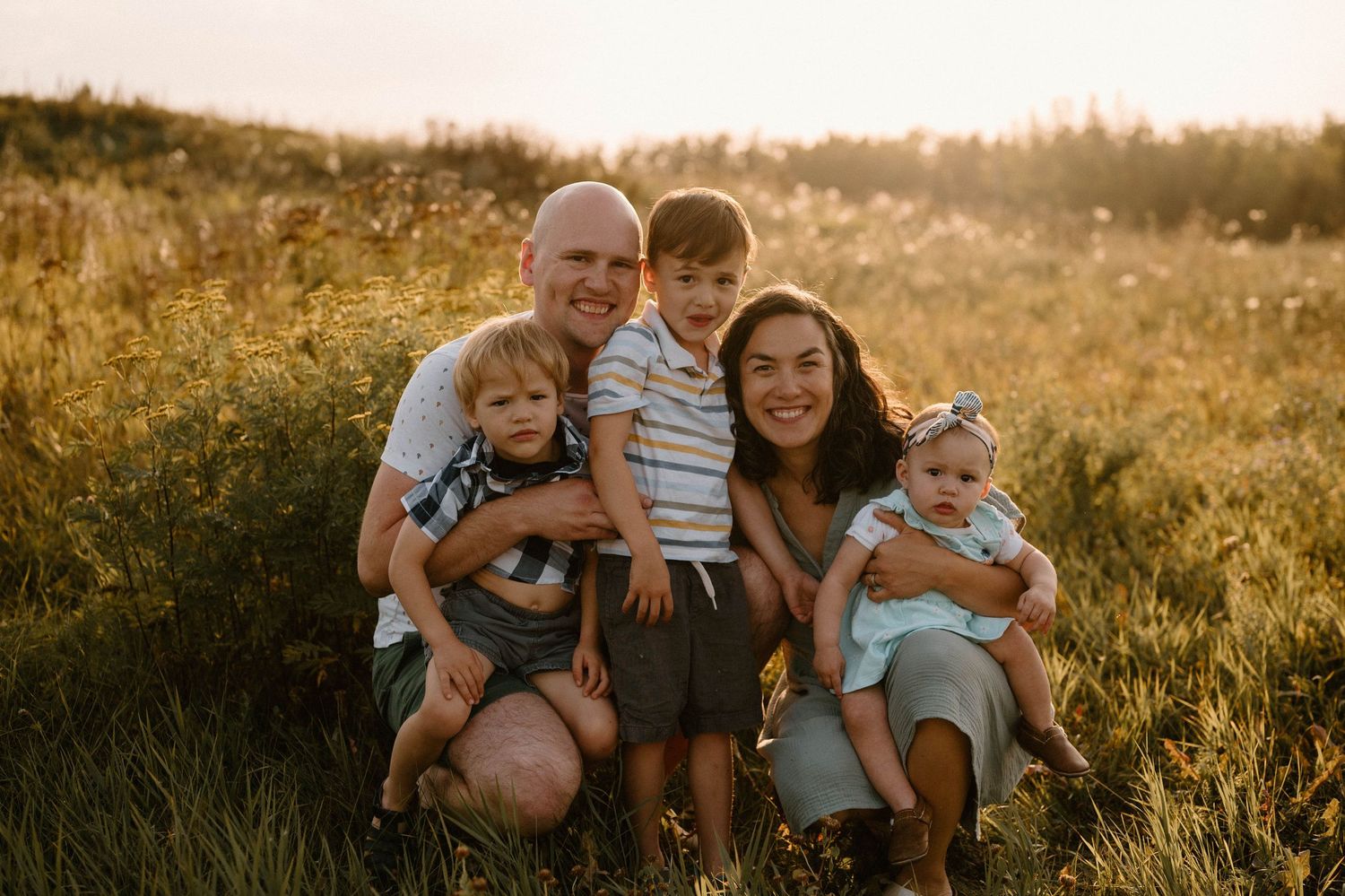 Happy family of five posing in golden hour sunlit field with wildflowers.