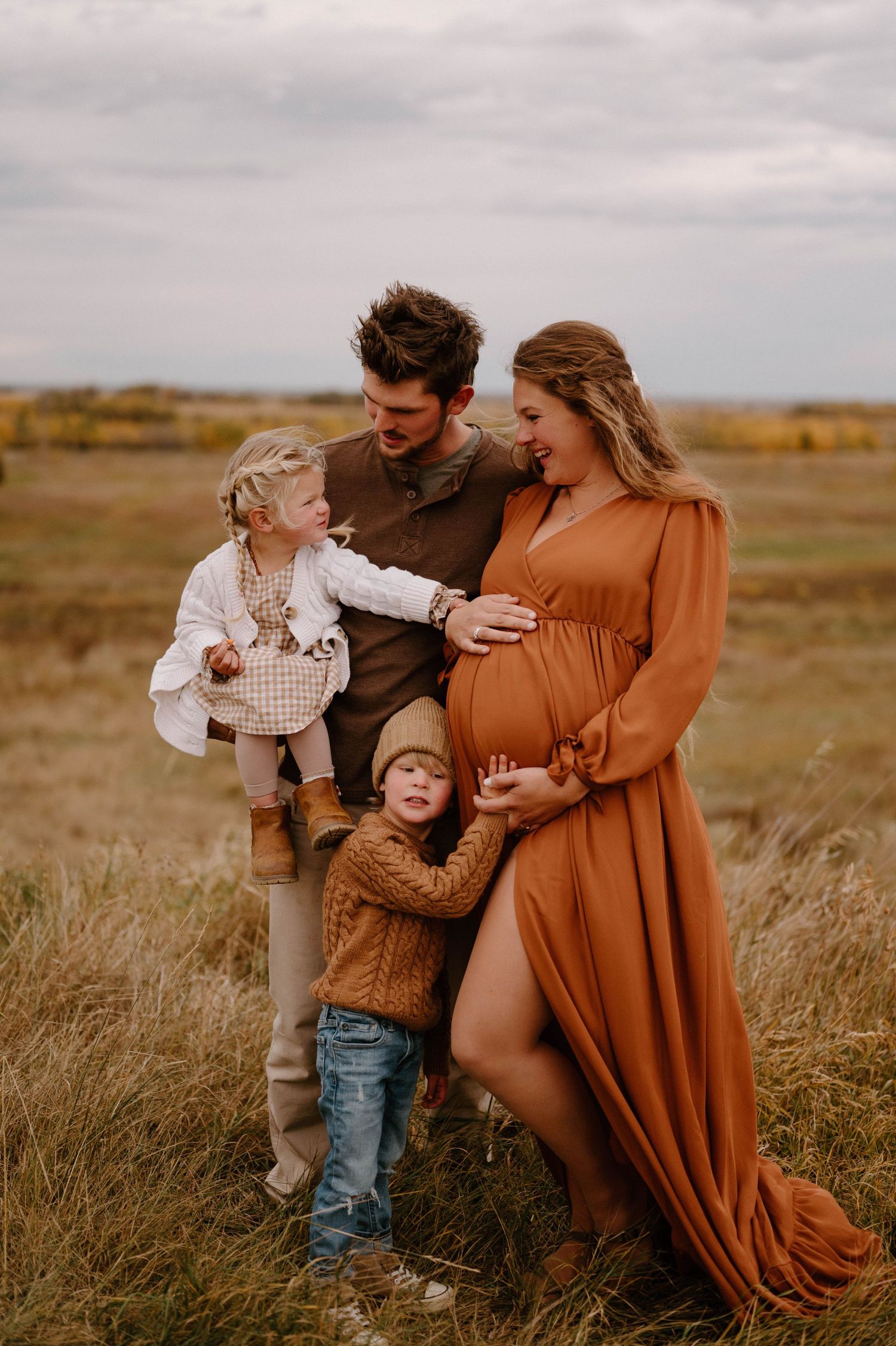 A family of four poses in Leduc, mother in a rust maternity dress cradling her bump.