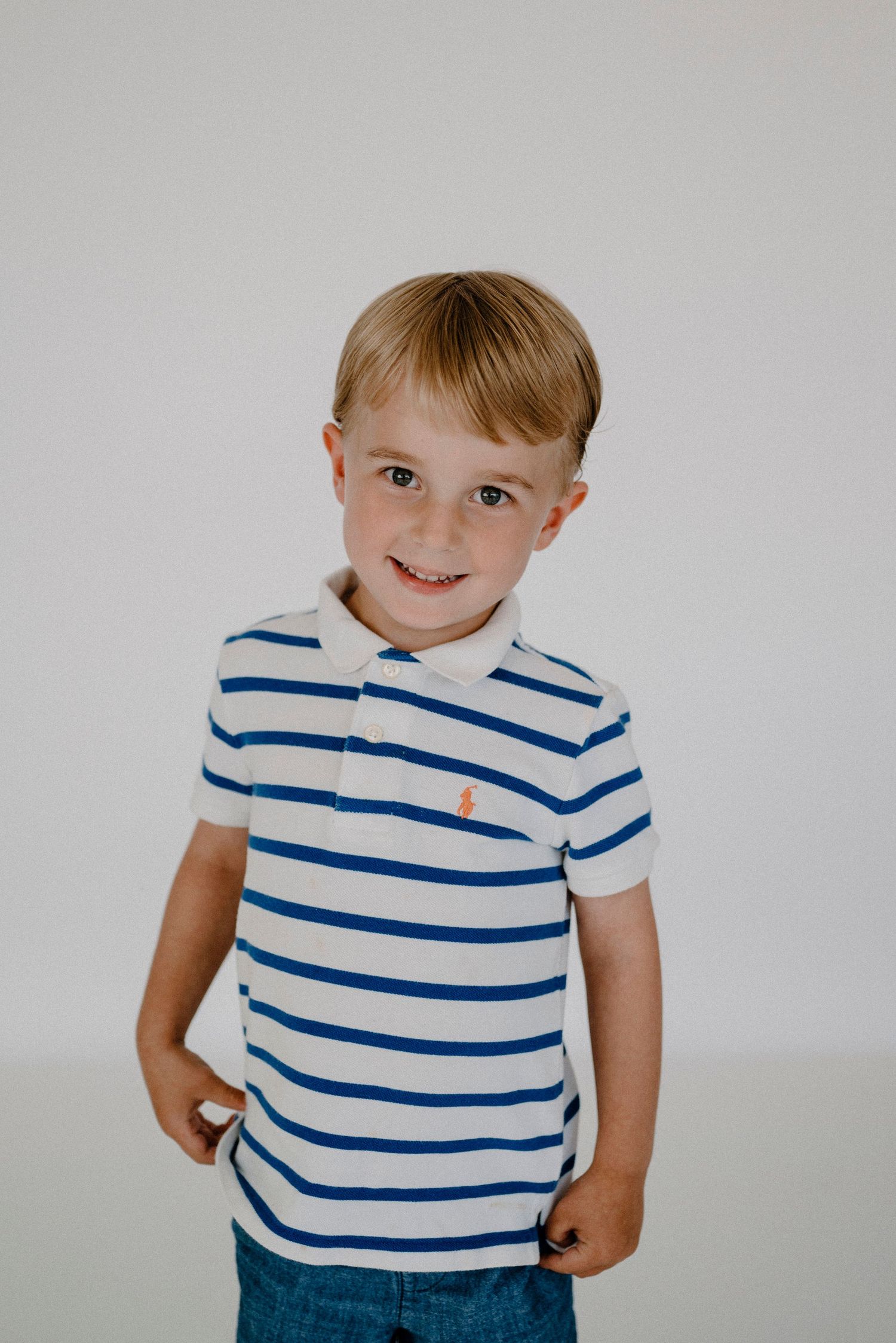 Smiling young boy in a blue and white striped Ralph Lauren polo shirt posing against a white background.