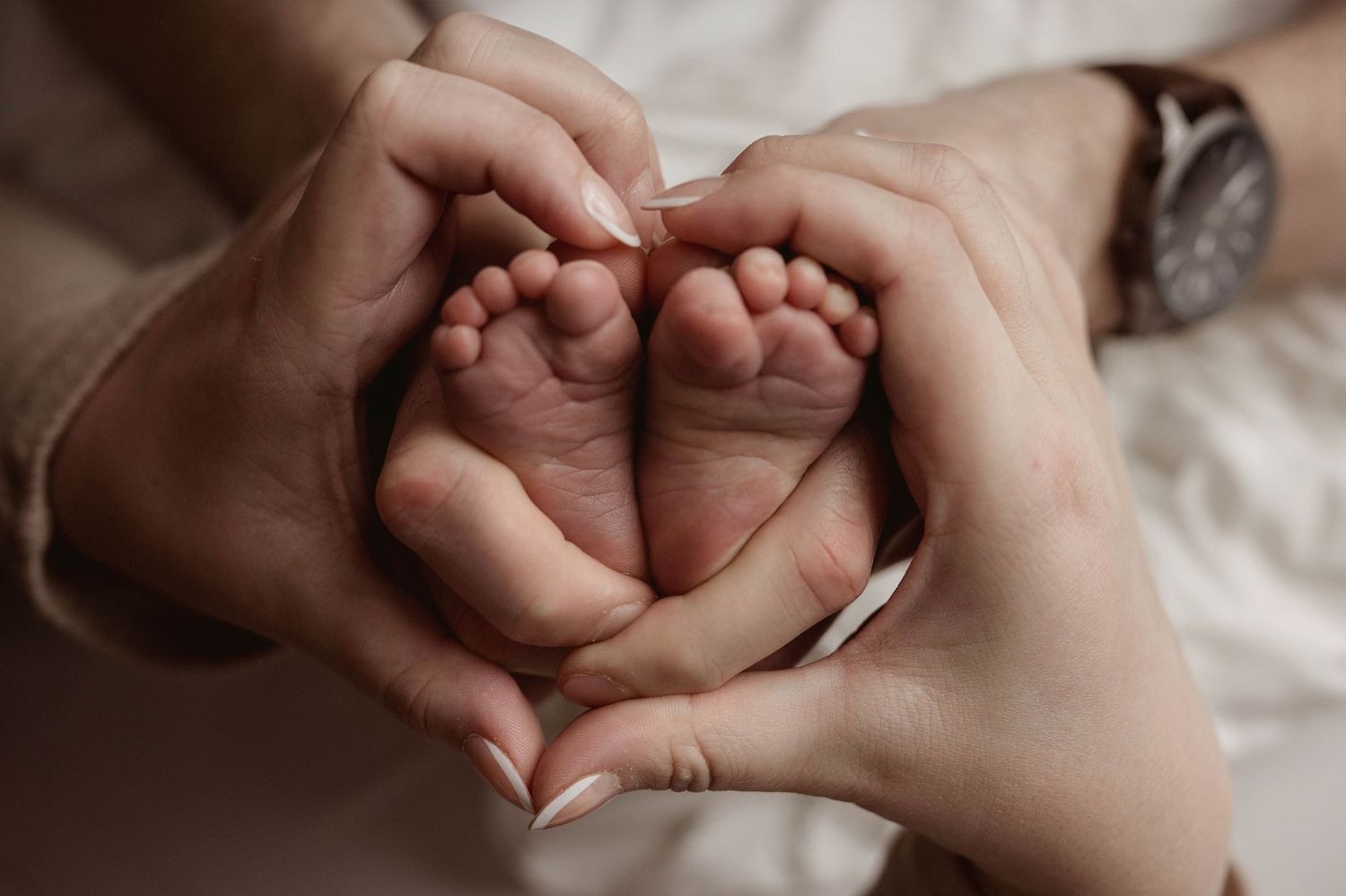 Parents forming a heart shape with their hands around their newborn baby's tiny feet.